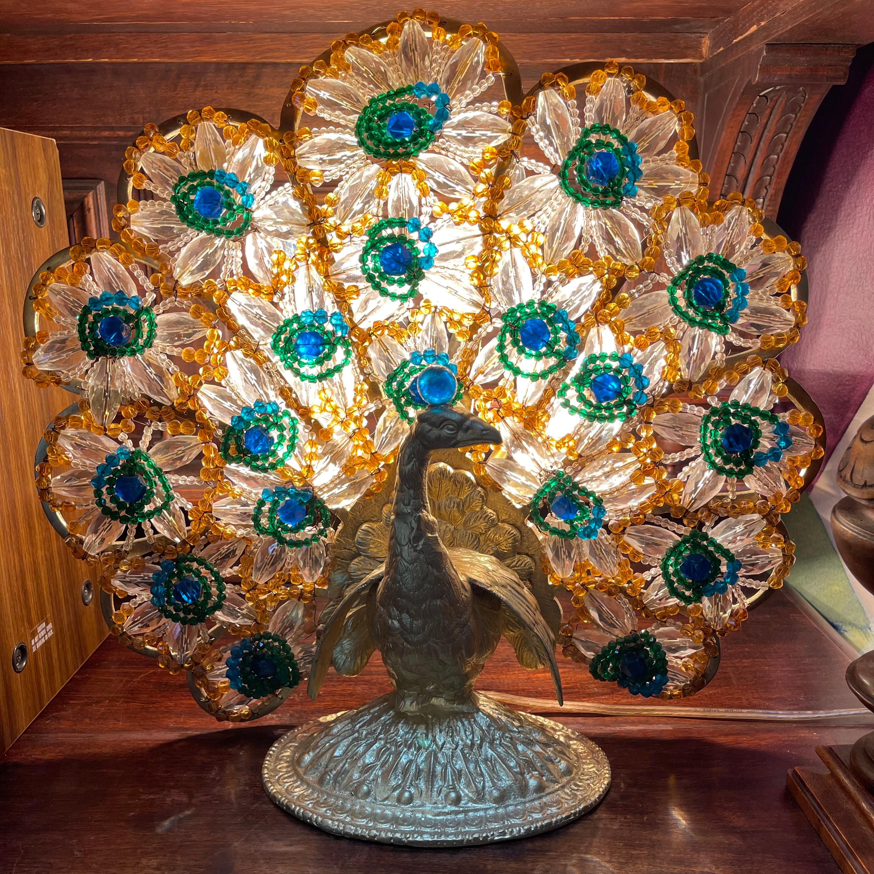Antique Hollywood Regency Bohemian beaded and gilt bronze peacock lamp.

This bohemian beaded and gilt bronze peacock lamp has a foliate cast base. The tail feathers are made from beaded glass in clear, amber, emerald green, and cobalt