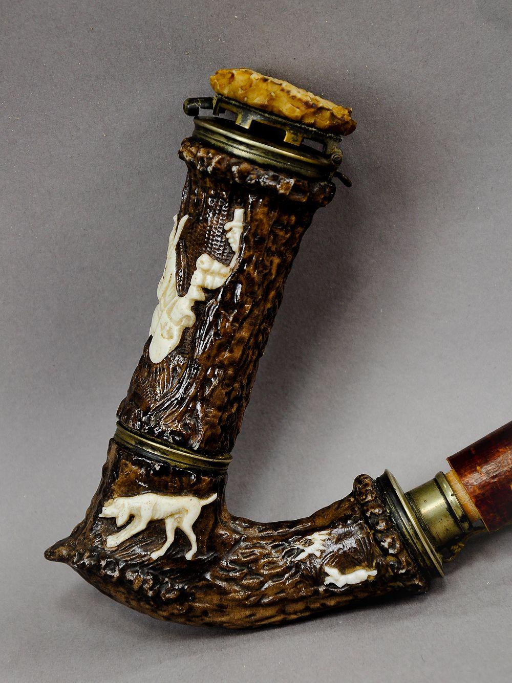 A hunters pipe made of porcelain. With surface-mounted hunting scenes like stags, wild birds, hunting dog and a poacher which steels the game from the sleeping hunter. On the lid a fine carved horn rose which shows a running deer. Executed, circa