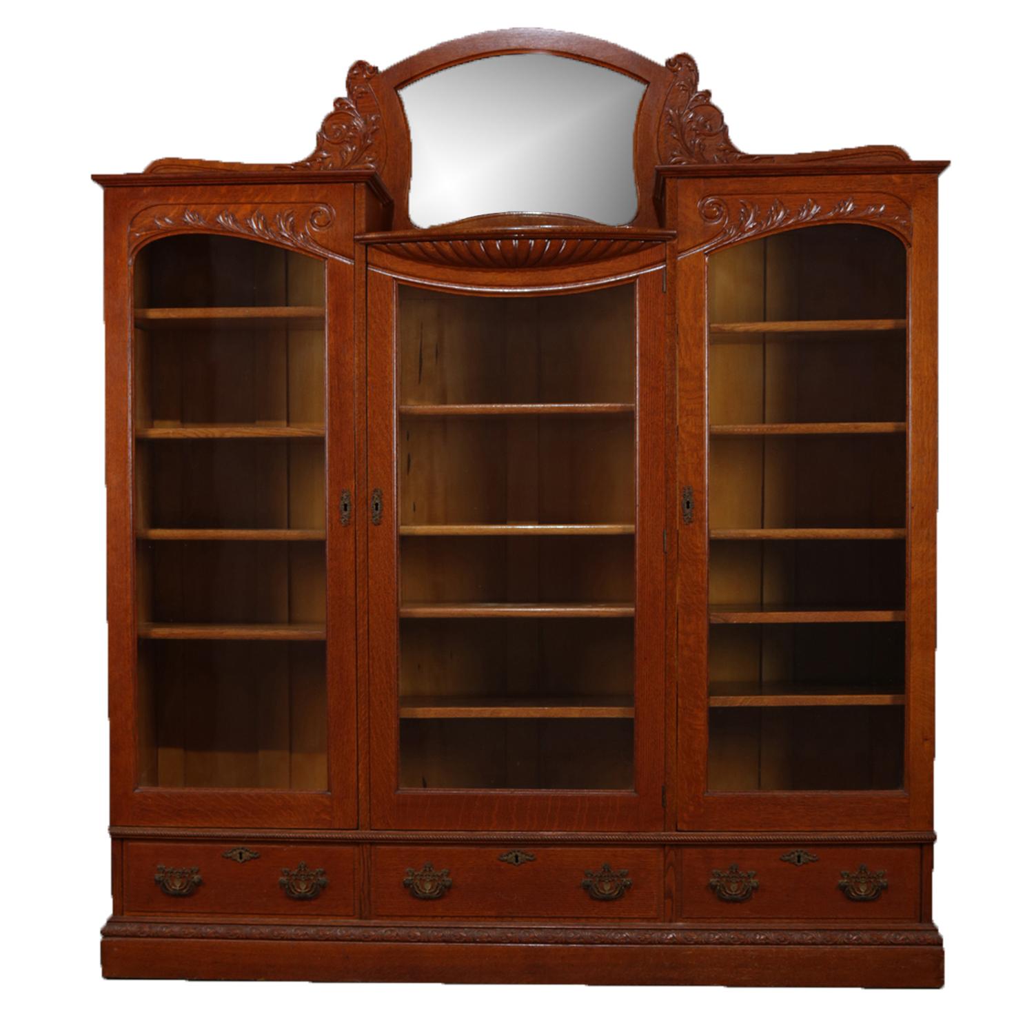 Antique Horner school bookcase features crest with central mirror and flanking carved foliate frame above three locking glass door bookcase with key and adjustable shelving and three lower locking drawers, circa 1900.

Measures: 73