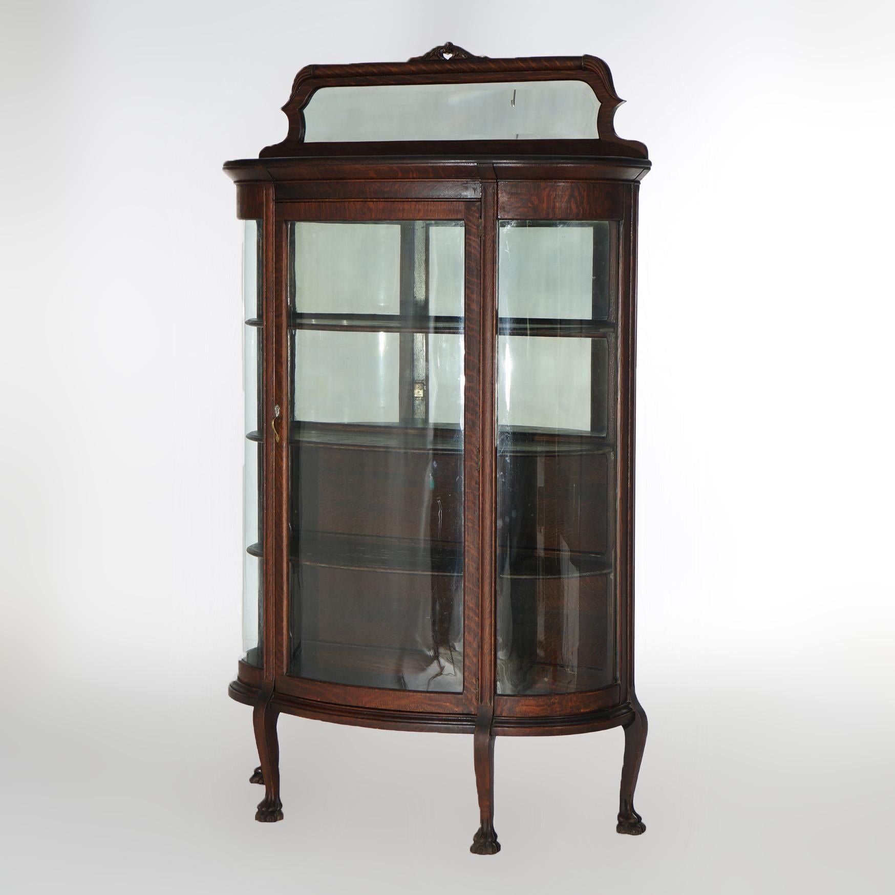 An antique china cabinet in the manner of Horner offers quarter sawn oak construction with mirrored backsplash having foliate carved crest over curved glass case having single door opening to mirrored and shelved interior, raised on cabriole legs