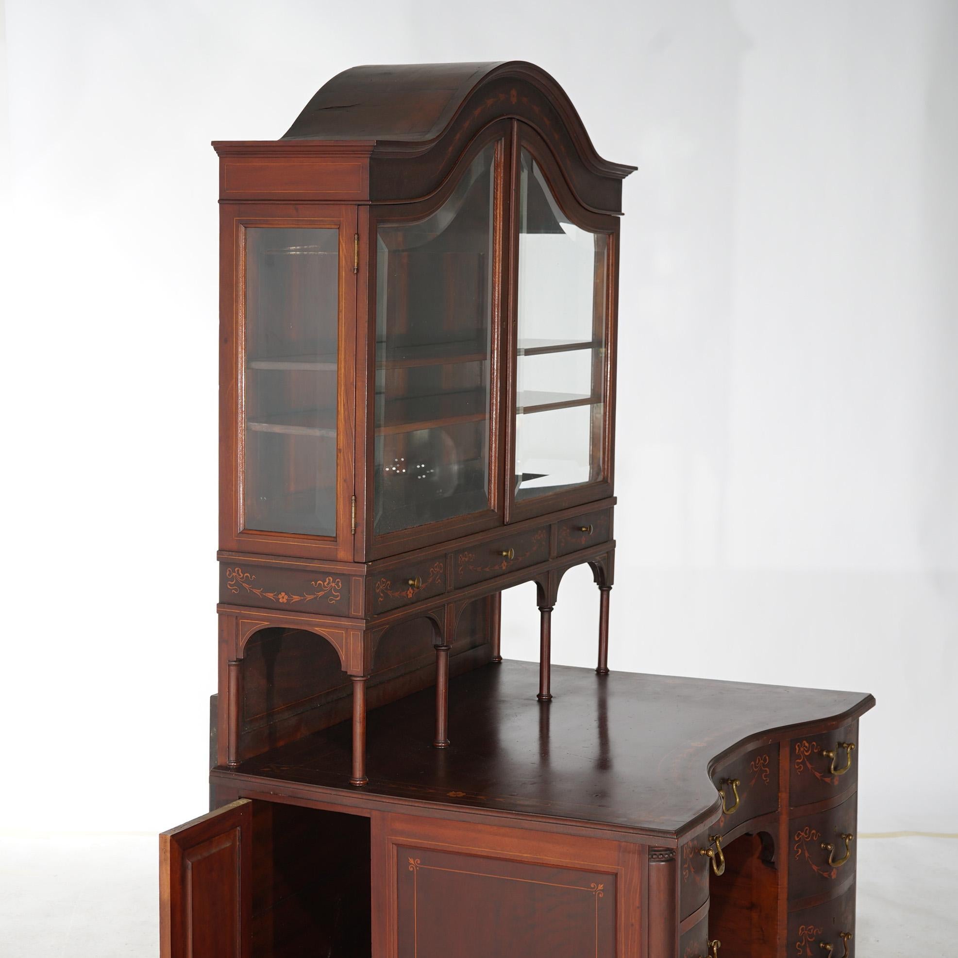 An antique secretary in the manner of Horner offers mahogany construction with upper having glass enclosed display in arched form with inlaid satinwood floral elements throughout, over lower with paneled case having drawers and cabinet with