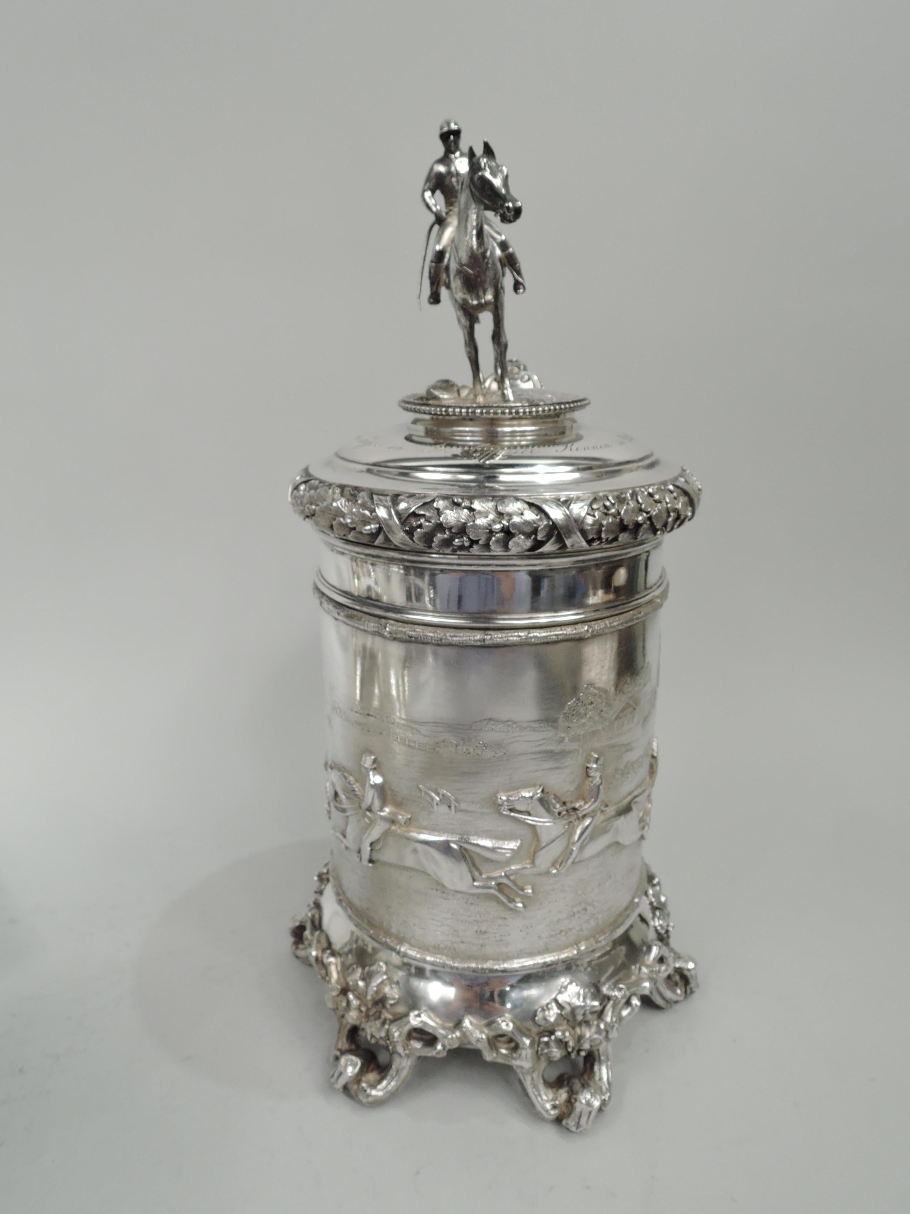 Equestrian-themed silver tankard with German imperial association, ca 1875. Straight and paneled sides with low-relief frieze depicting galloping riders, racing through the countryside, trees and buildings in the background; branch borders.