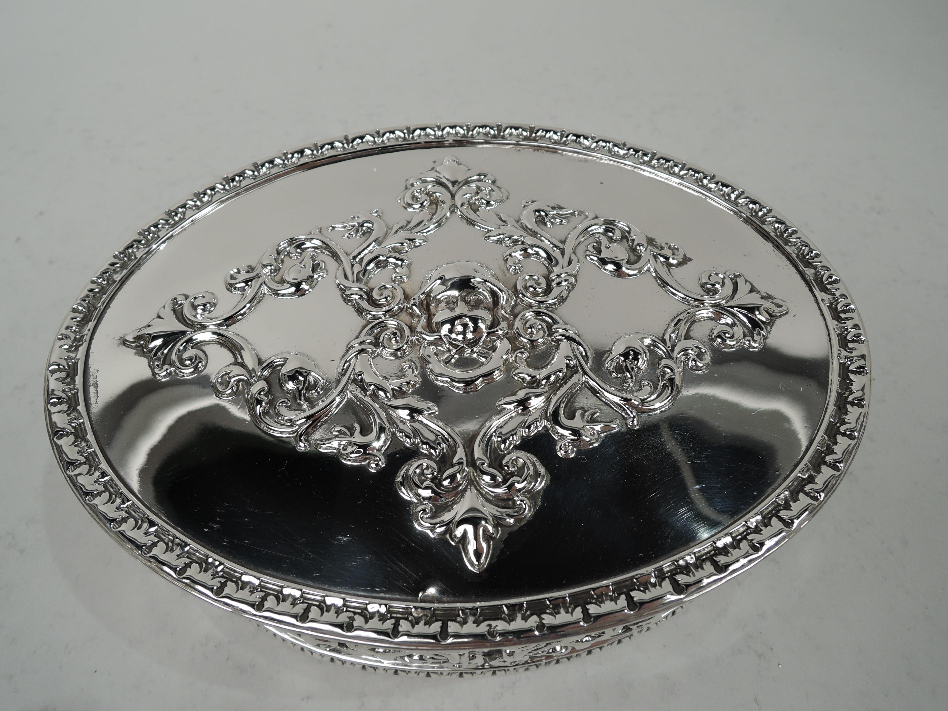 Edwardian Classical sterling silver trinket box. Made by Howard & Co. in New York in 1901. Oval with straight sides and flat hinged cover. Leafing scrollwork applied to sides and cover top, which also has centrally mounted cherub’s head. Reeded rims
