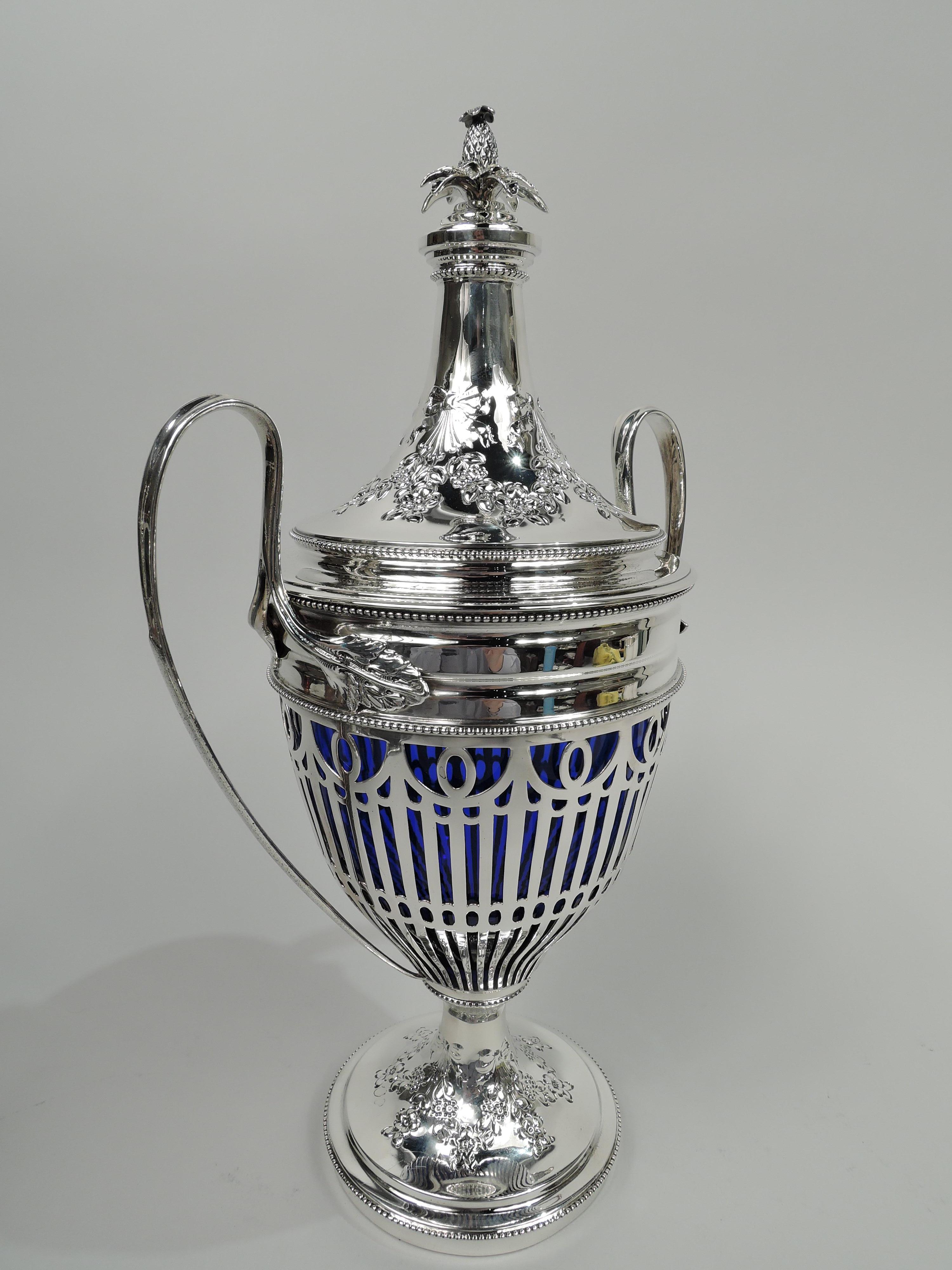 Edwardian Neoclassical sterling silver covered urn. Made by Howard & Co. in New York, ca 1900. Ovoid bowl with high-looping leaf-mounted side handles; domed foot. Cover domed; top stepped with cast pineapple finial. Sides open with flutes and
