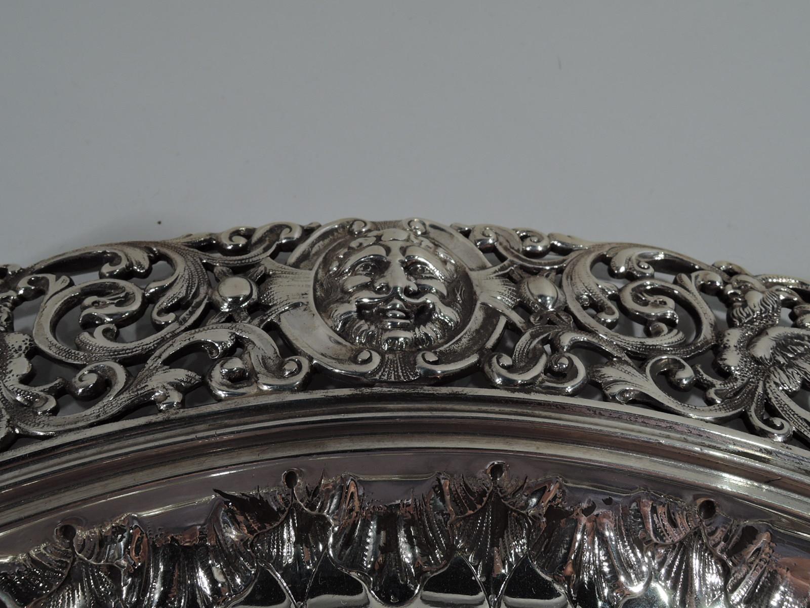 Renaissance-Revival sterling silver tray. Made by Howard & Co. in New York in 1890. Round and deep well with chased leaf-and-dart border. Wide and pierced rinceaux rim entwined with gryphons and flowers, and interspersed with raised Classical masks.