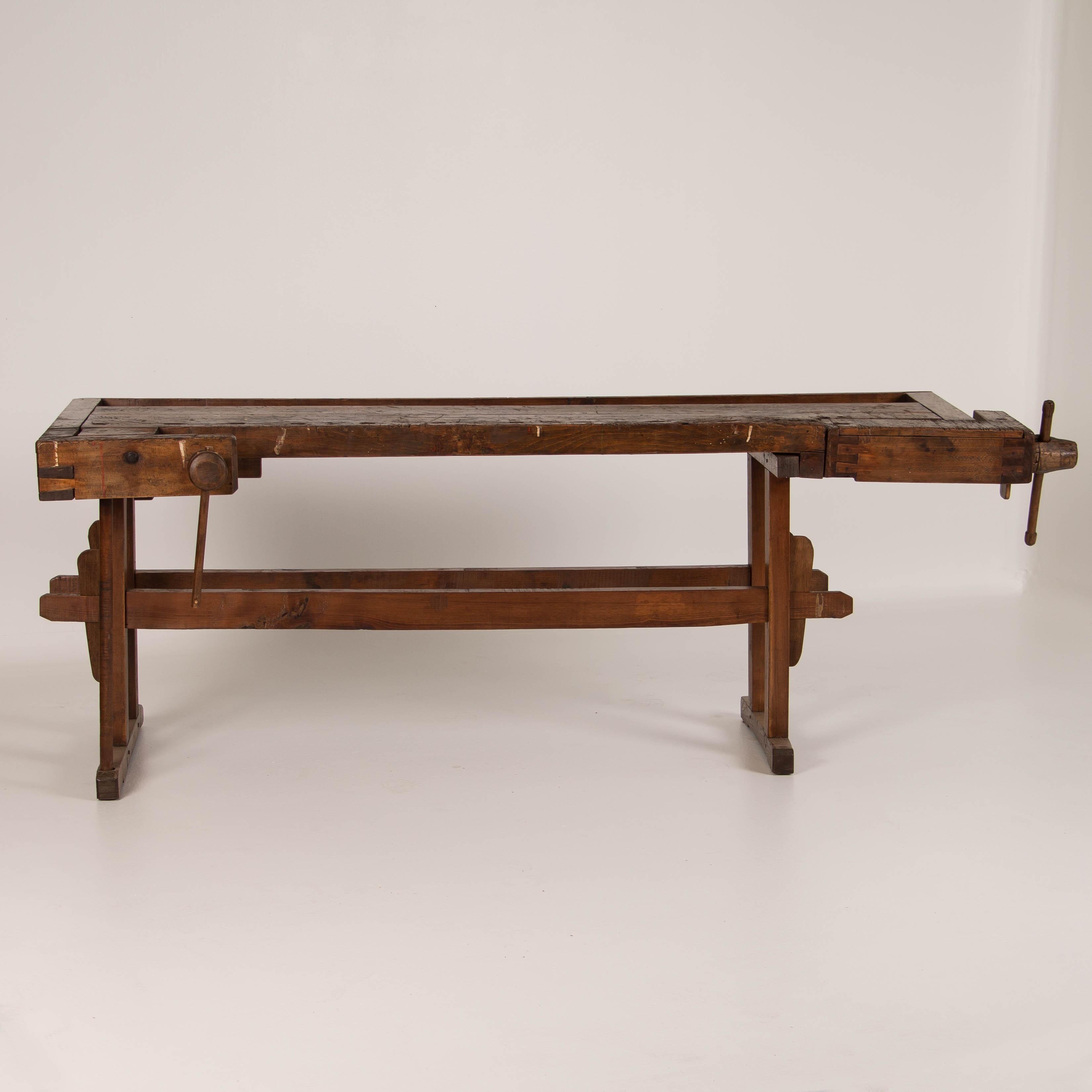 The depth of patina on this workbench comes from years of constant use. It has two wooden vices and a recessed tray where the carpenter would lay his tools. The traditional trestle base allowed it to be assembled and taken down/moved more easily.