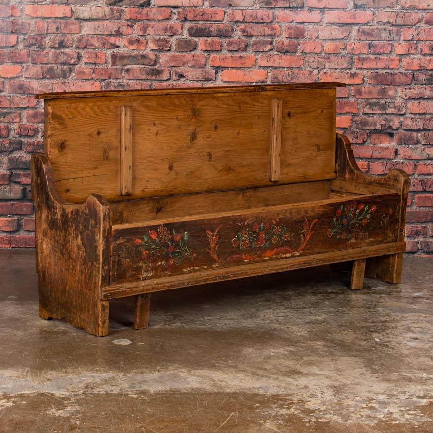 This quaint storage bench from Hungary still maintains its original painted floral patterns and rich earth tones that embellish the bench in the Folk Art style of the late 19th and early 20th century. The hinged seat, with the paint worn away from