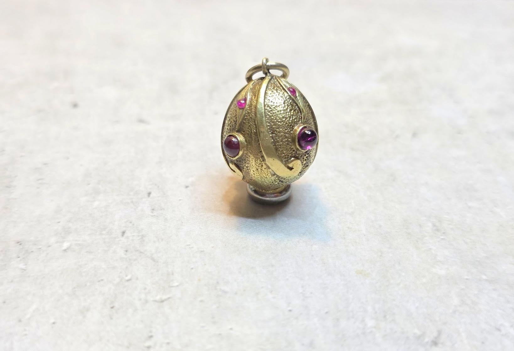 Presenting a rich and finely egg pendant adorned with foliage ornamentation encrusted with four garnets and four tiny rubies. The body of the egg features hand-engraved yellow polished and brushed gold that creates a fantastic contrast. It is truly