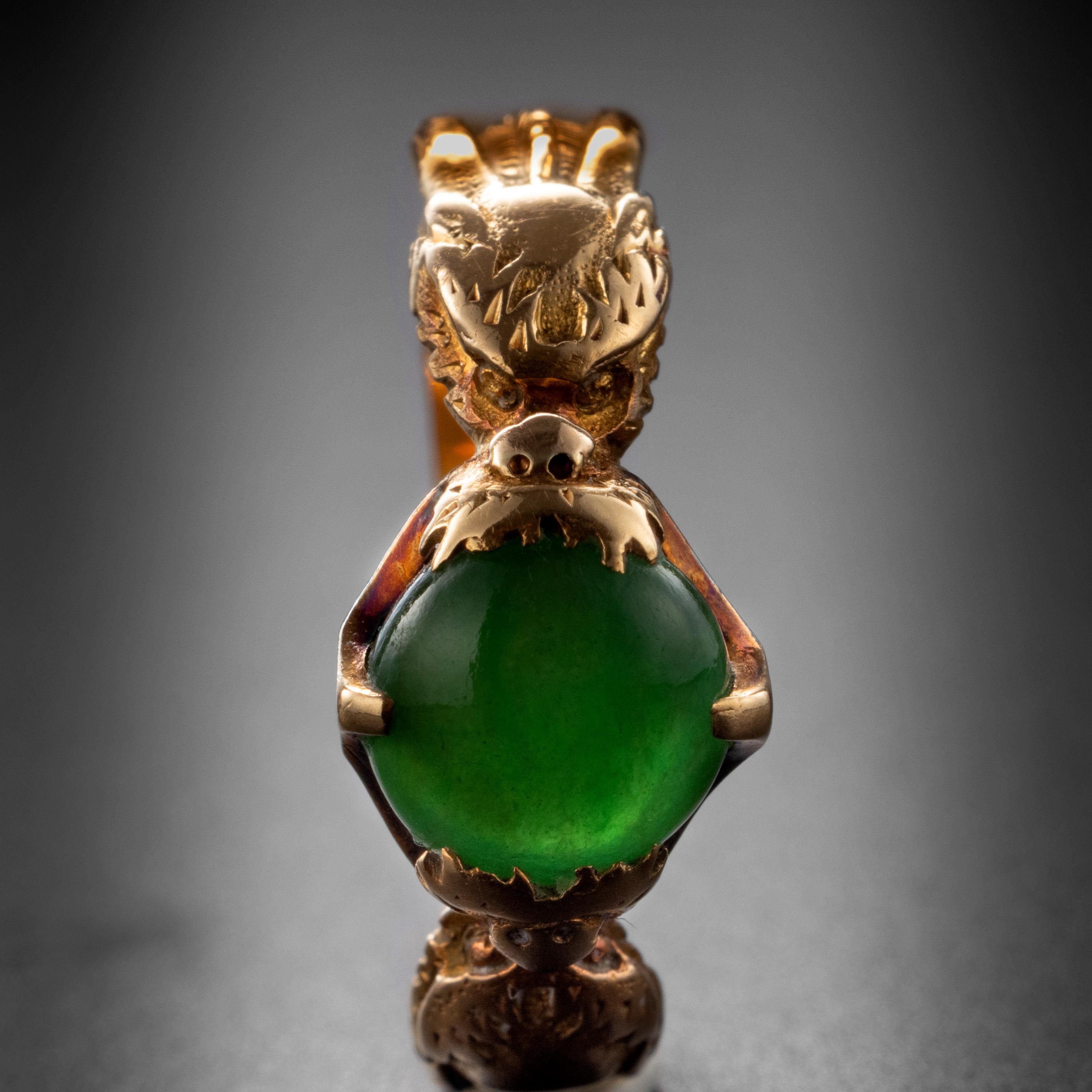 A round double-cabochon of fine emerald-green jade is gripped within the jaws of two figural dragons in this beautiful and whimsical antique Chinese ring from the late 1800s. The vivid green jade is so translucent that it appears to absorb and
