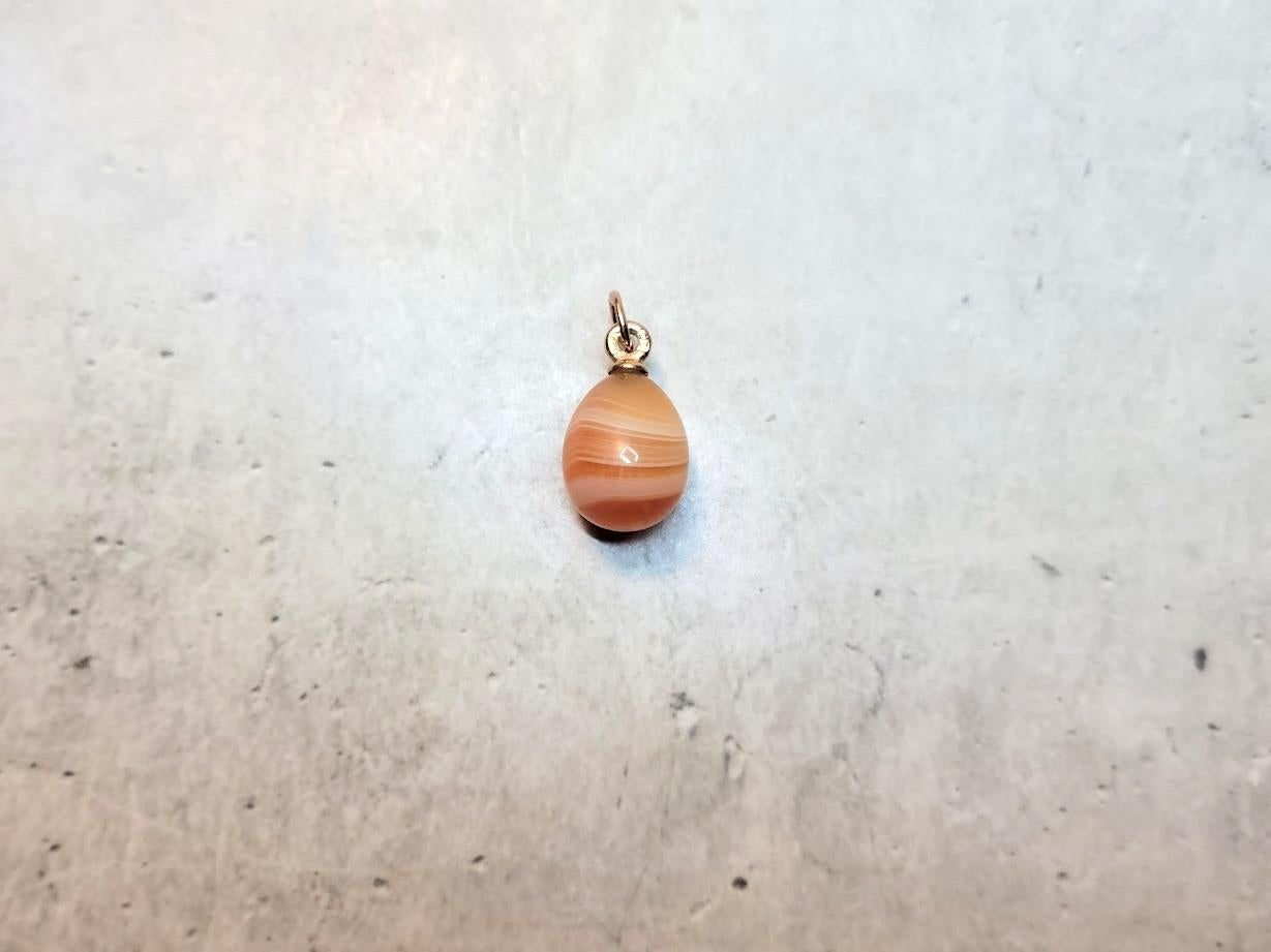 We present to you an exquisite miniature egg-shaped pendant crafted from orange lace agate and rose gold. This unique piece was created by Livonian jeweler Phillip Theodor Ringe, who worked in the workshops of the House of Fabergé, which was made in