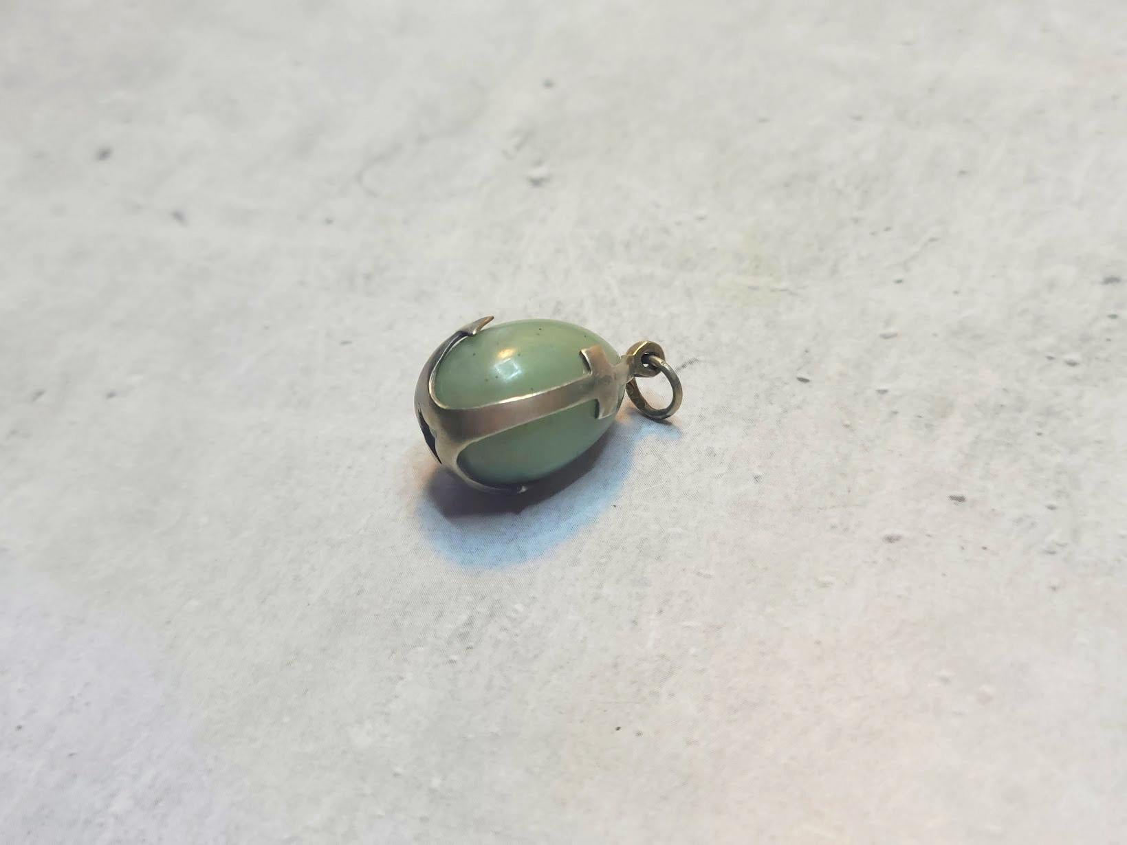 Ti presentiamo un incantevole ciondolo antico a forma di uovo in giada naturale intagliata a mano, ornato da una cornice in argento dorato a forma di ancora.

Il corpo dell'uovo è realizzato in argento russo imperiale dorato, contrassegnato dal