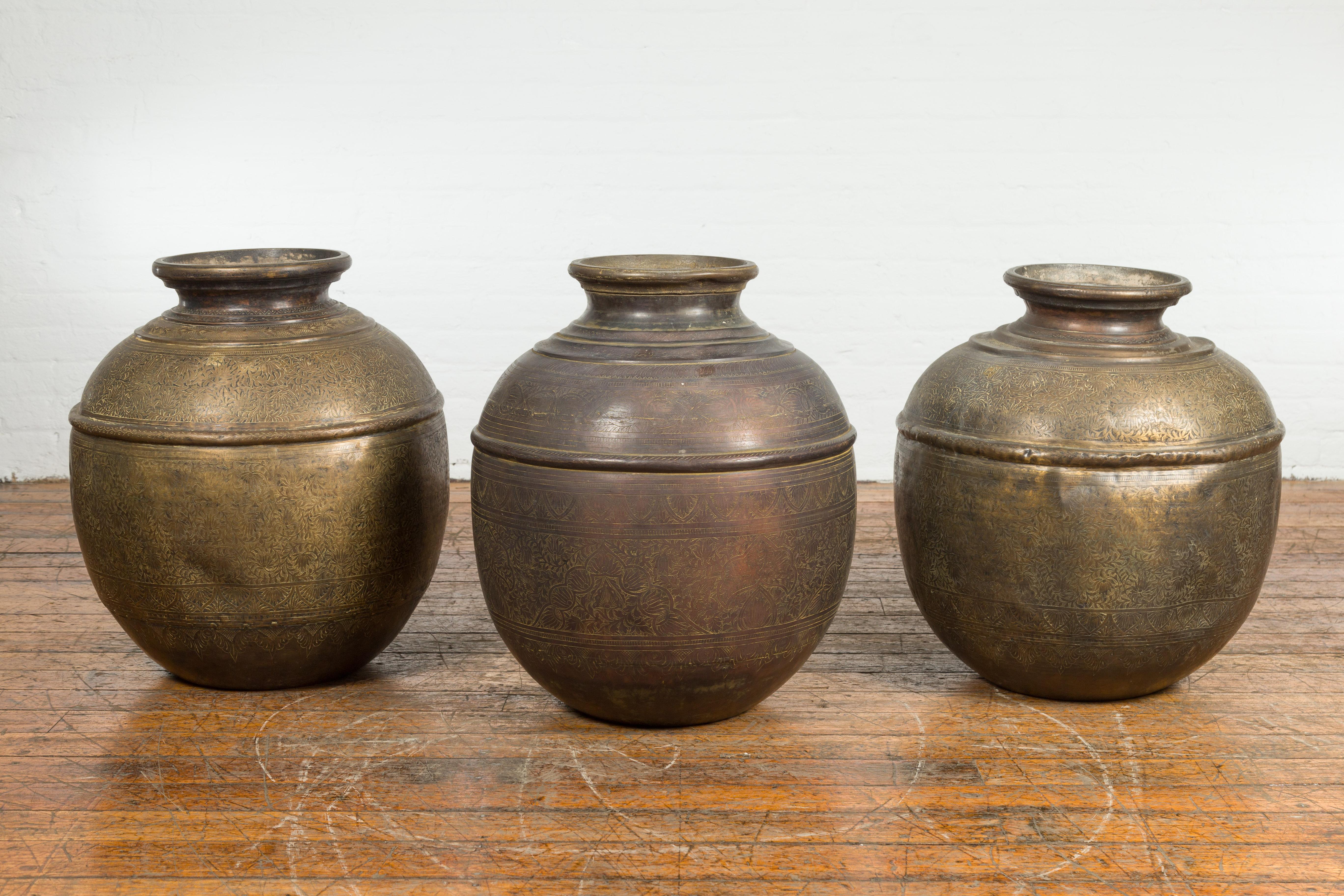 Trois vases à eau indiens anciens en laiton du 19e siècle, avec un décor floral gravé et un aspect usé par le temps. Nous fixons le prix et vendons ces produits individuellement. Créés en Inde au XIXe siècle, ces grands récipients d'eau en laiton