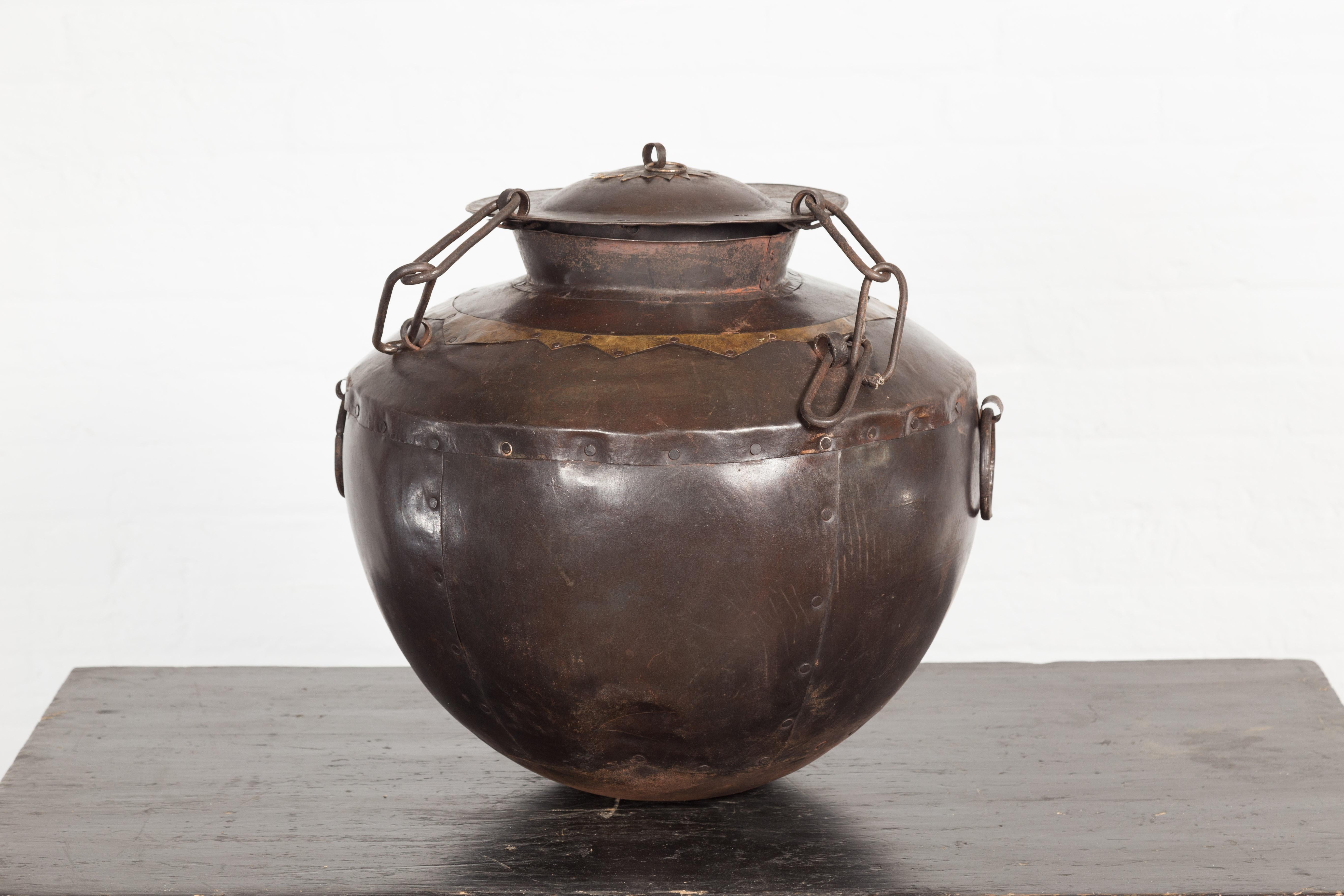 An antique Indian iron lidded water vessel from the 19th century with brass geometric accents and tapering lines. This alluring antique Indian iron lidded water vessel from the 19th century is a captivating blend of history, craftsmanship, and