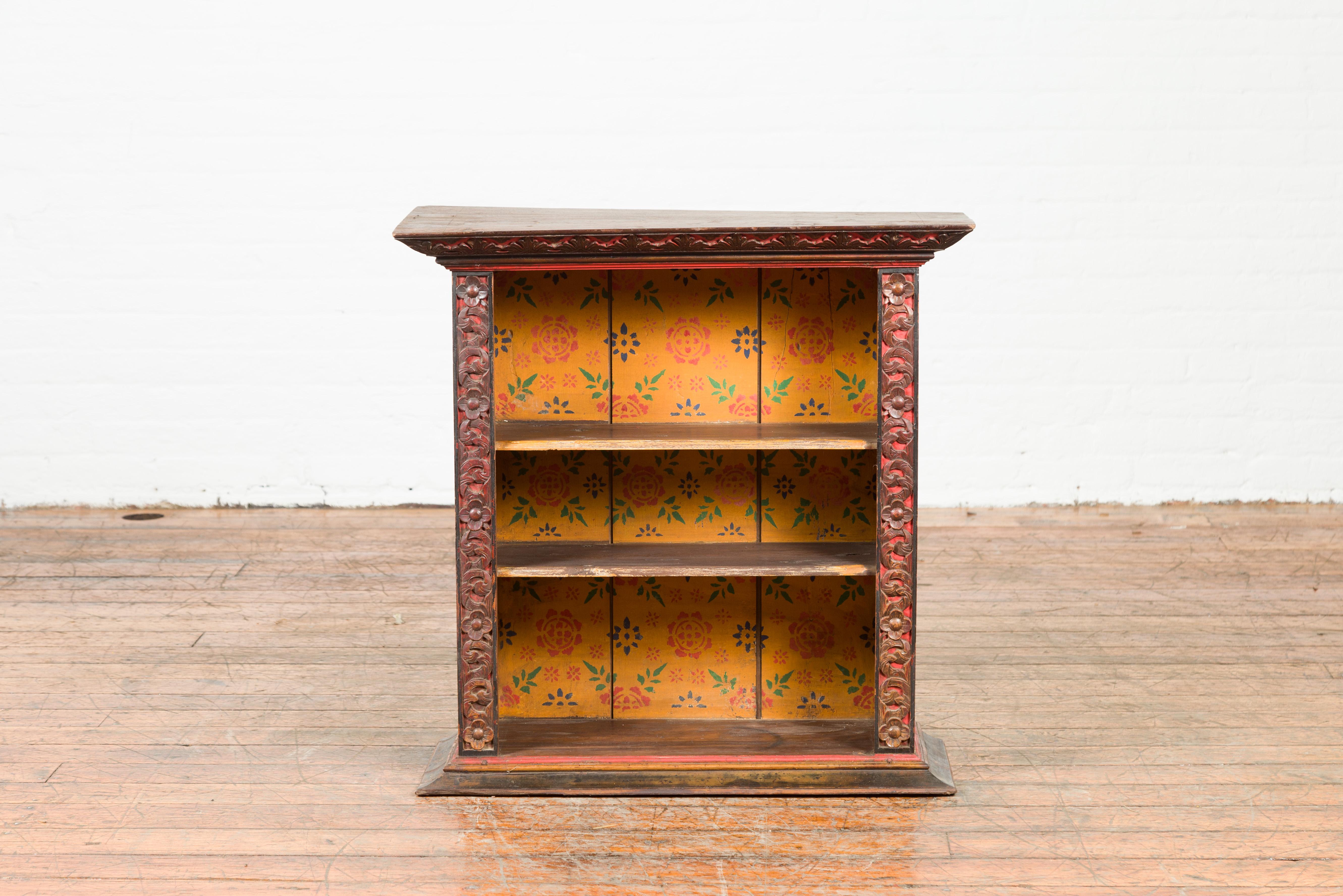 An Indian antique wall display cabinet from the 19th century, with carved floral motifs and polychrome accents. Created in India during the 19th century, this display cabinet features a large beveled cornice overhanging a façade made of open shelves