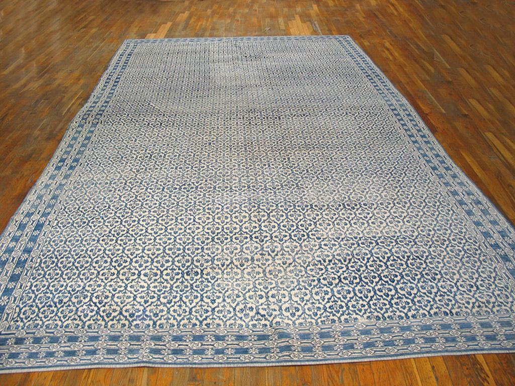 Interwar cotton Agra carpets often employ bi-tonal palettes, especially off white and medium blue, as here, with a very small honeycomb lattice whose cells each enclose a simplified four leaf plant. Five denim blue and ecru borders with star