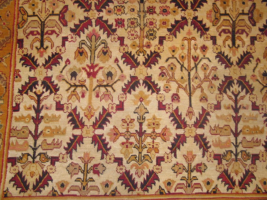 This a definitely antique northern Indian Agra carpet with a sand field showing an allover pattern of a broken lattice formed of small, oblique leaves enclosing a variety of somewhat angular flowers. Chocolate main border of reversing flowers in two