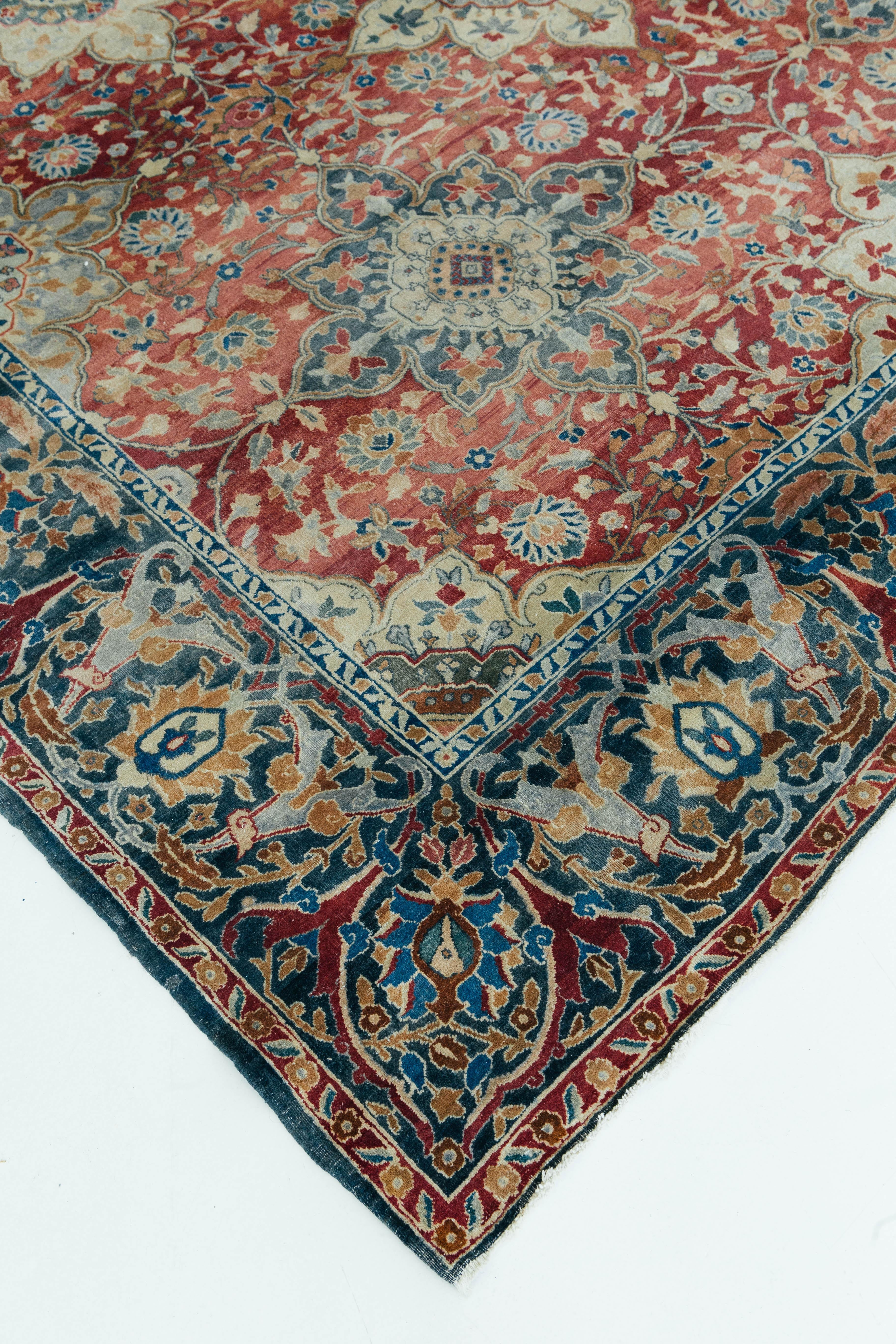 A antique Indian Agra rug from the Uttar Pradesh region of Northern India. This beautiful oversized rug is a well preserved antique piece with beautiful red, blue, and ivory hues. Together these colors create beautifully detailed floral patterns