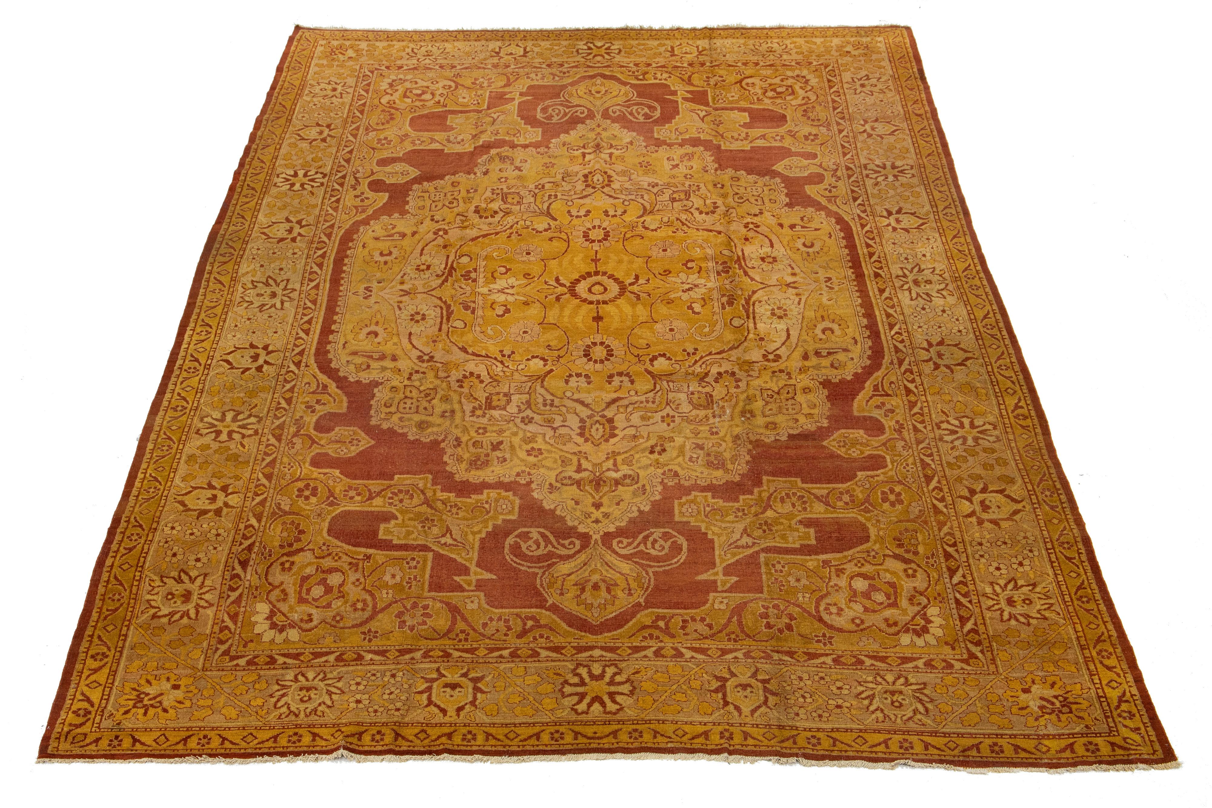 Dieser handgeknüpfte Wollteppich aus Amritsar zeigt einen atemberaubenden goldroten Hintergrund, der mit einem verschlungenen rost- und hellbraunen Blumenmedaillon verziert ist. Dieses exquisite Stück verbindet auf wunderbare Weise die exotische