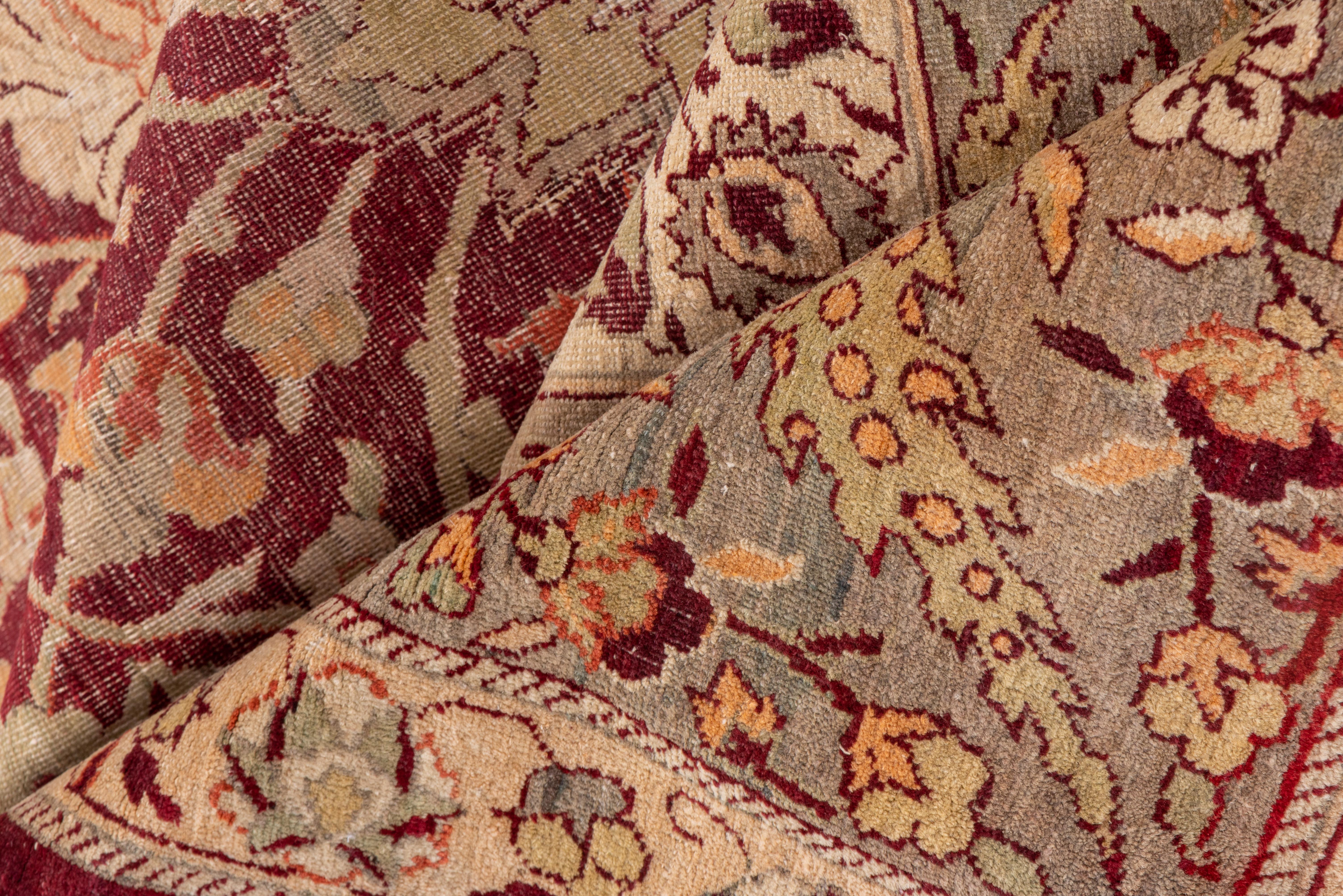 Ce tapis de ville du nord de l'Inde présente un champ rouge lie-de-vin orné d'une palmette arrondie, d'une rosette et d'un court motif d'arabesque fourchue en 