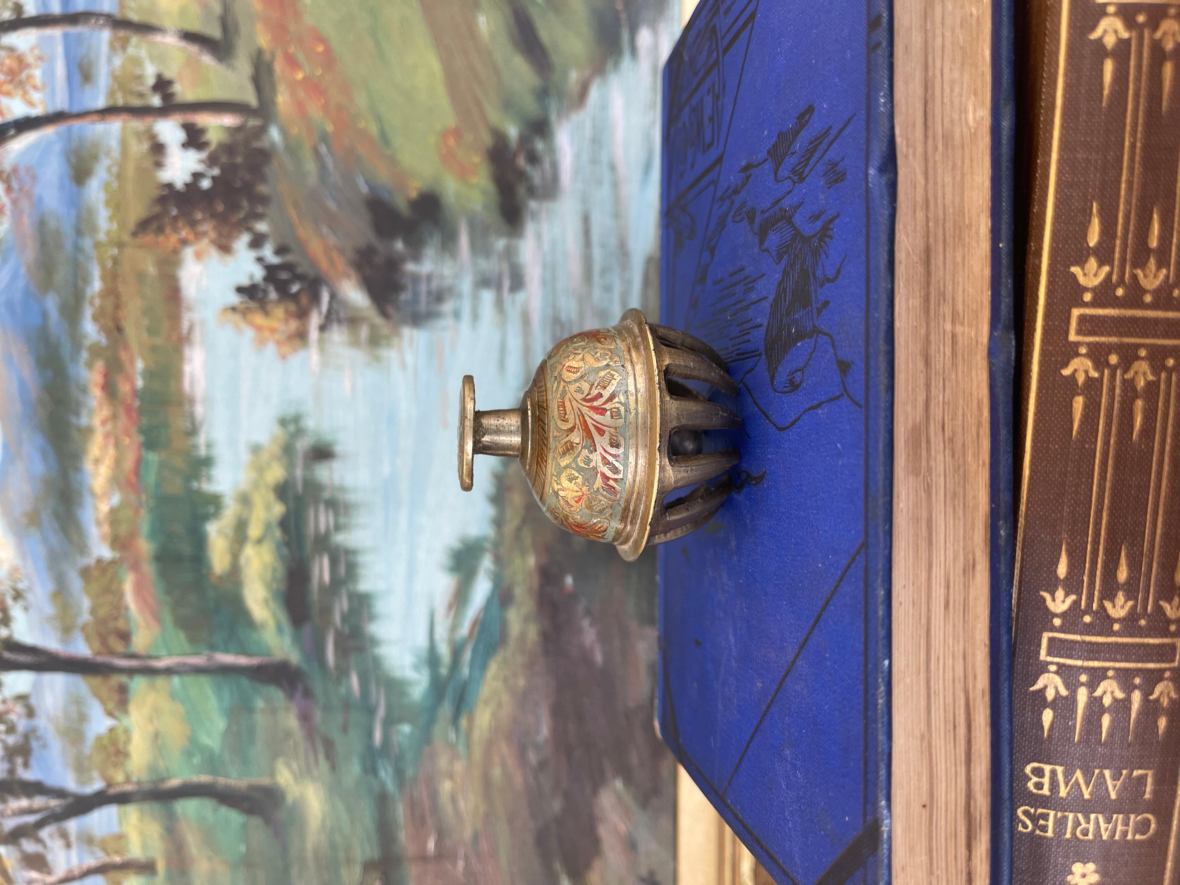 Questa campana a mano indiana, probabilmente antica, è probabilmente realizzata in ottone massiccio e presenta una caratteristica base a zampa d'artiglio e un corpo a cupola riccamente decorato con motivi floreali smaltati a mano in rosso, verde e