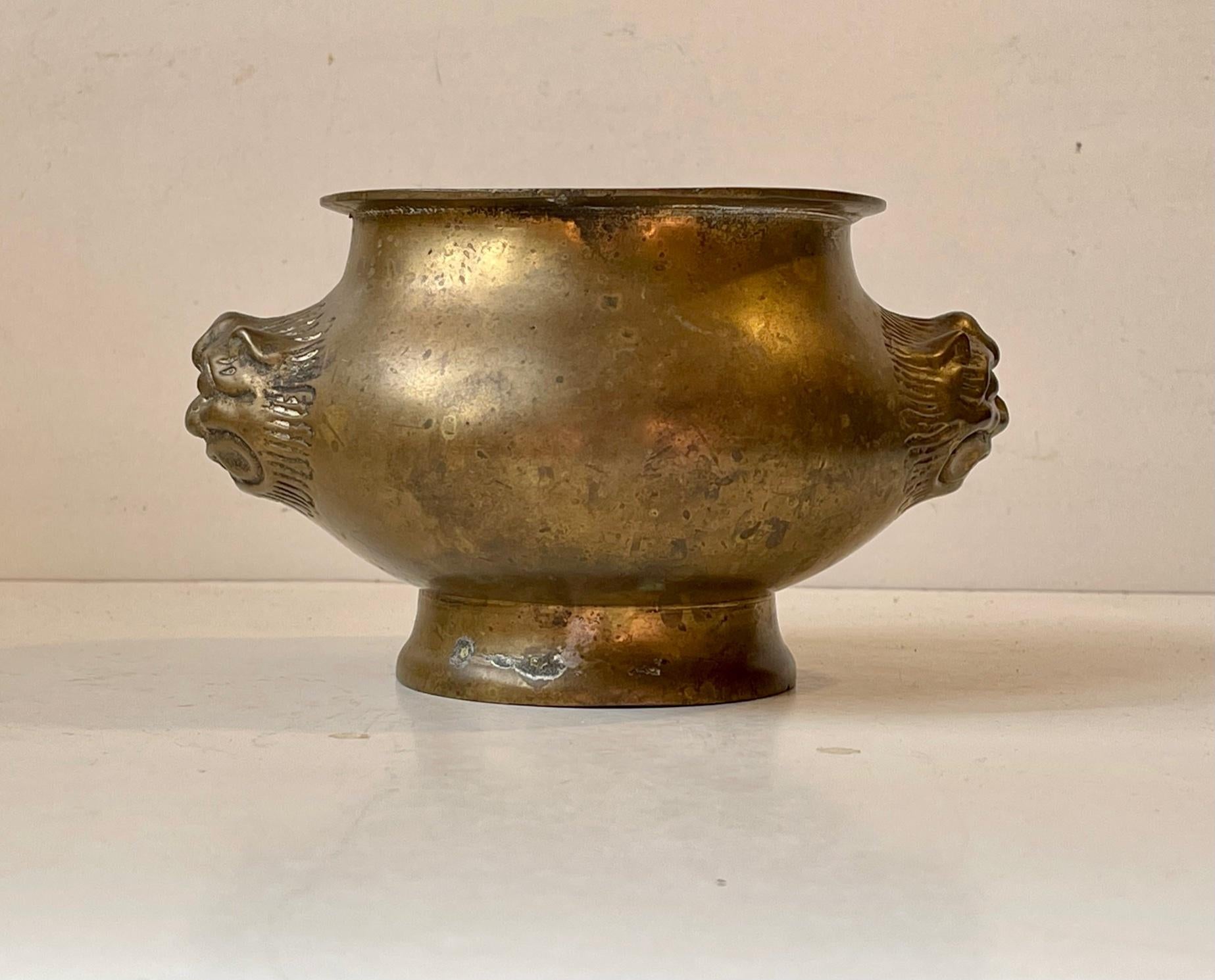 An Indian Lota or jardiniere/planter in patinated brass. It is cast and features hand engraved lion heads to each side. A great authentic piece of decor in any Yoga or Meditation environment. Artisan made in India in the late 18th or early 19th