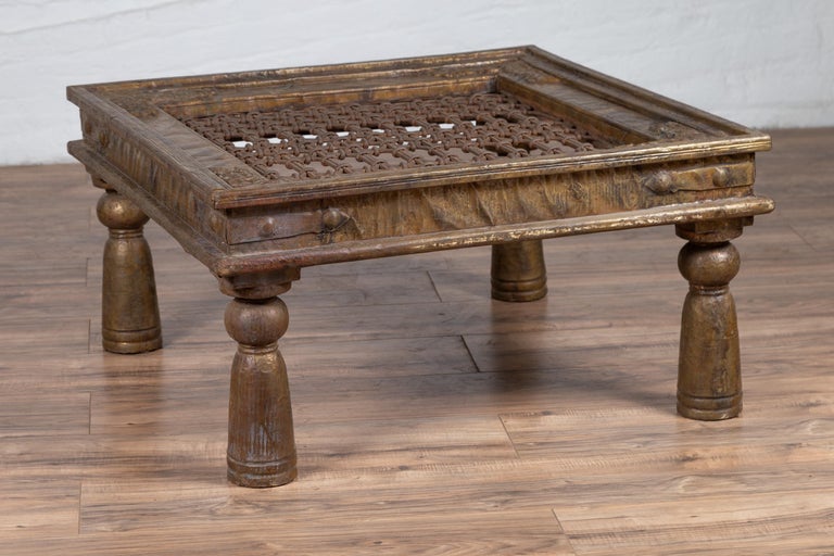 An Indian open iron design coffee table made of an antique brass window grate with iron geometric design top and delicate floral motifs. Born in India during the early years of the 20th century, this Indian window grate with geometric patterns is