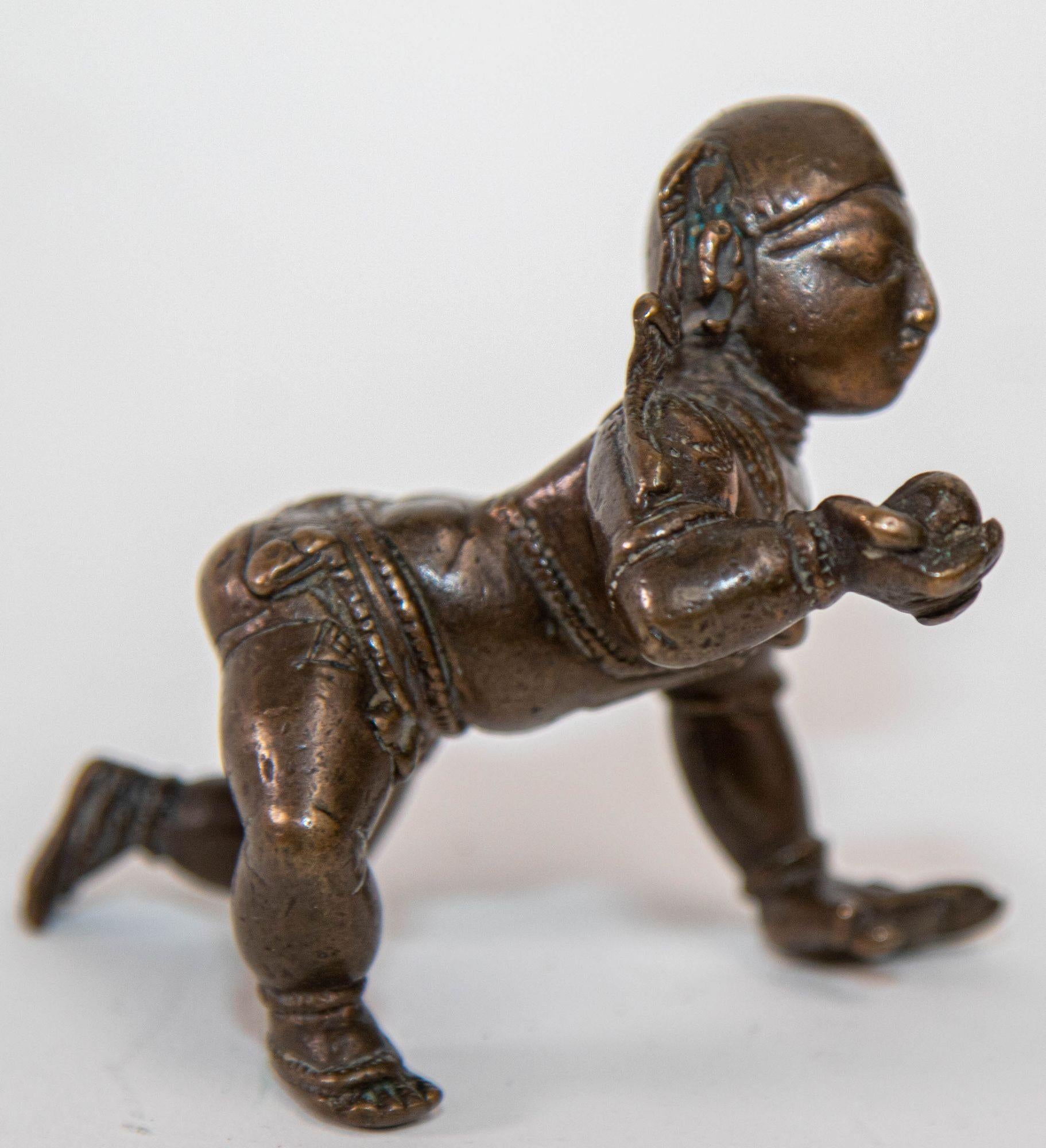 Antike Bronzefigur von Baby Bala Krishna krabbelnde Figur hält die Perle der Weisheit oder Butterball.

Eine indische Bronzefigur von Balakrishna, dem kleinen Krishna, der Ketten um seine Taille und eine Halskette trägt, sein Gesicht mit einem