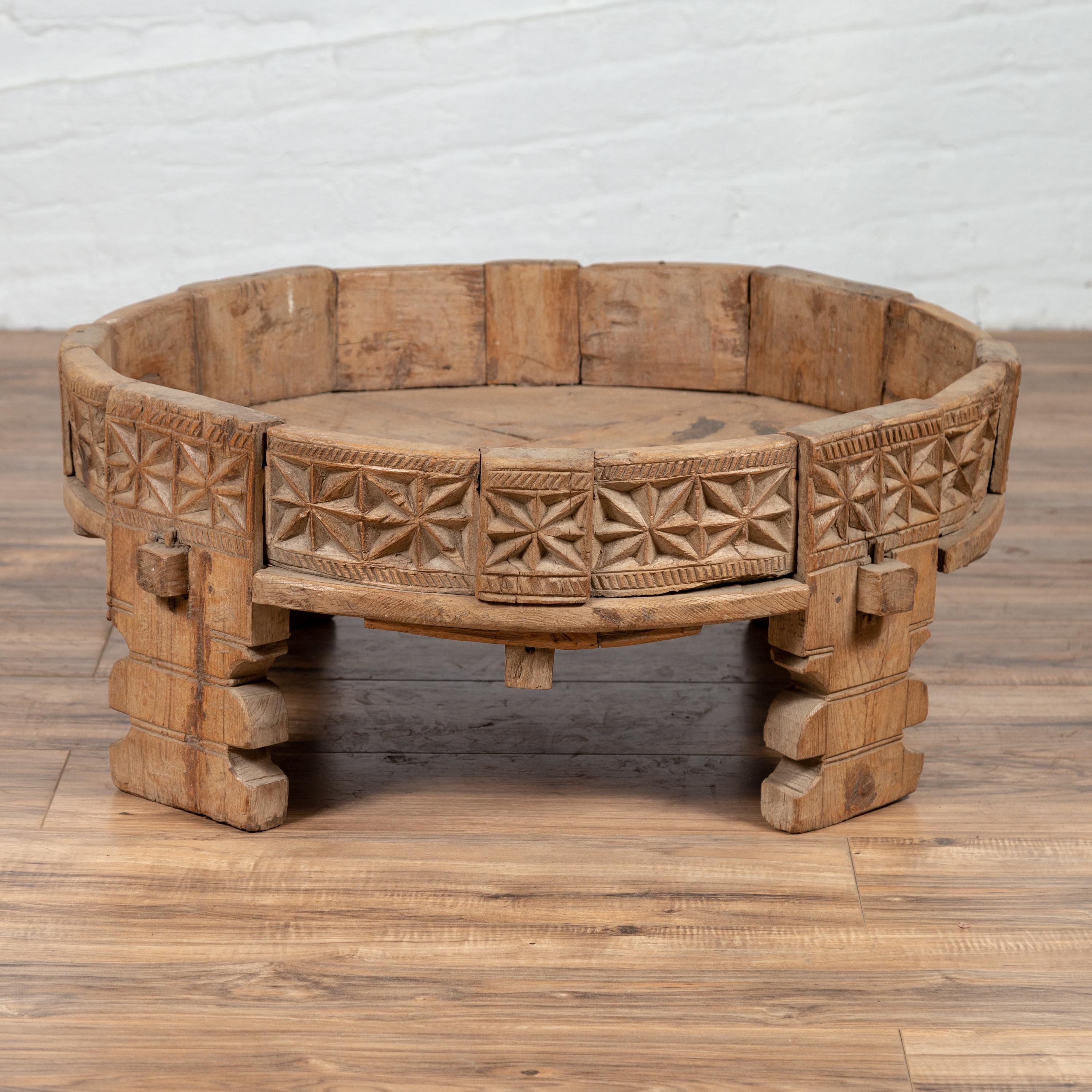 An antique Indian carved wooden grinding wheel made into a coffee table. Traditionally used to grind grains to flour before collecting for cooking, these wheels are richly decorated on their outer edge. Ours is adorned with geometrical patterns made