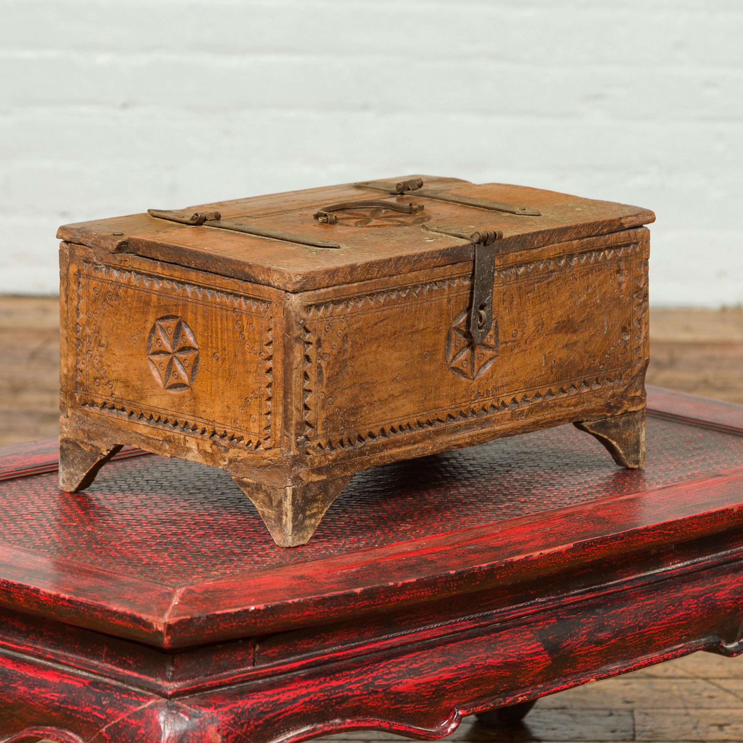 An antique Indian wooden box from the 19th century with carved rosettes and weathered appearance. Topped with a rectangular lid adorned with a central carved rosette echoed on the other sides, this old cash box is raised on bracket feet. Boasting a