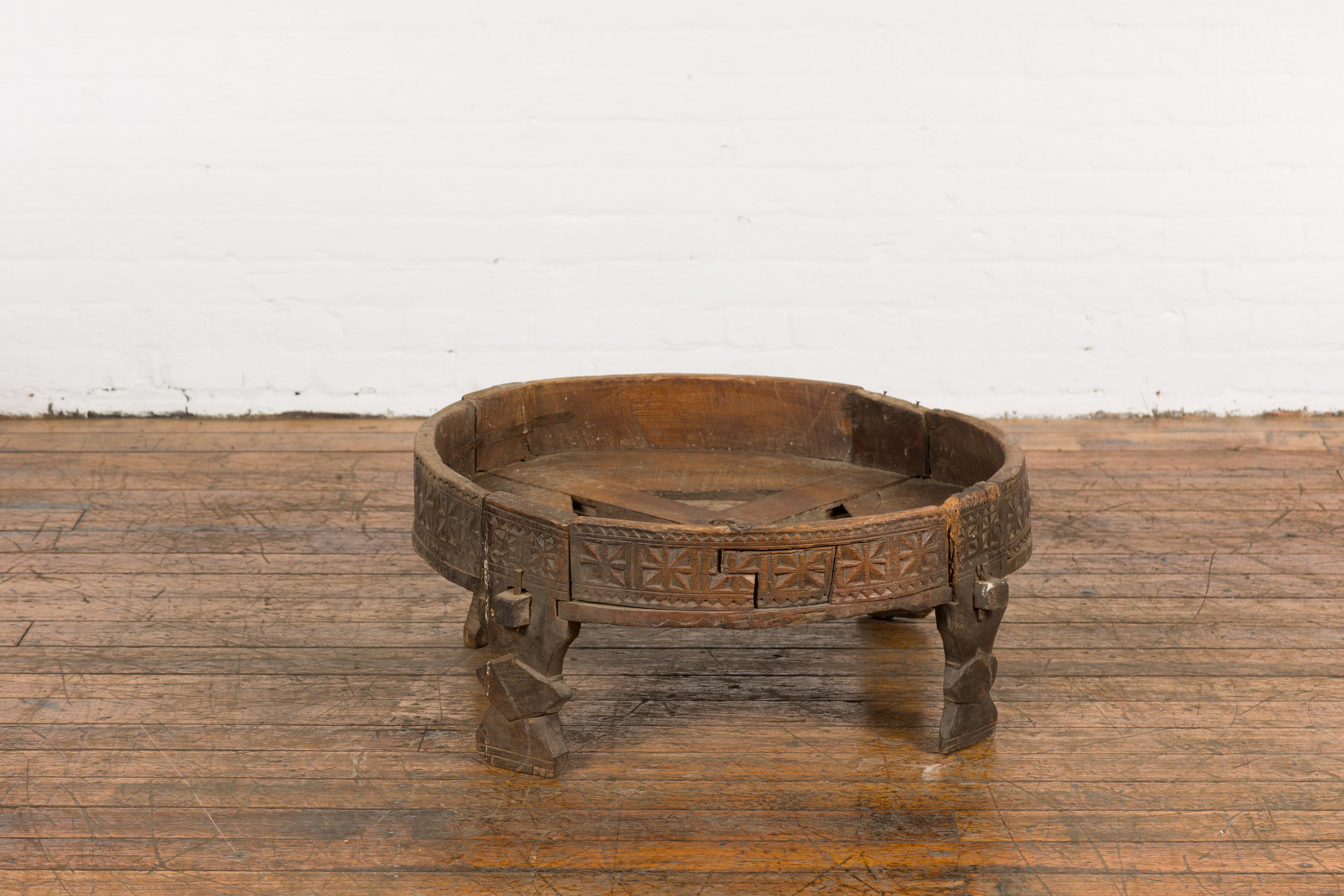 A Tribal Indian rustic Chakki grinder table from the early 20th century with hand-carved geometric motifs, open center, carved feet and weathered patina. Created in India during the early years of the 20th century, this grinder table is called a
