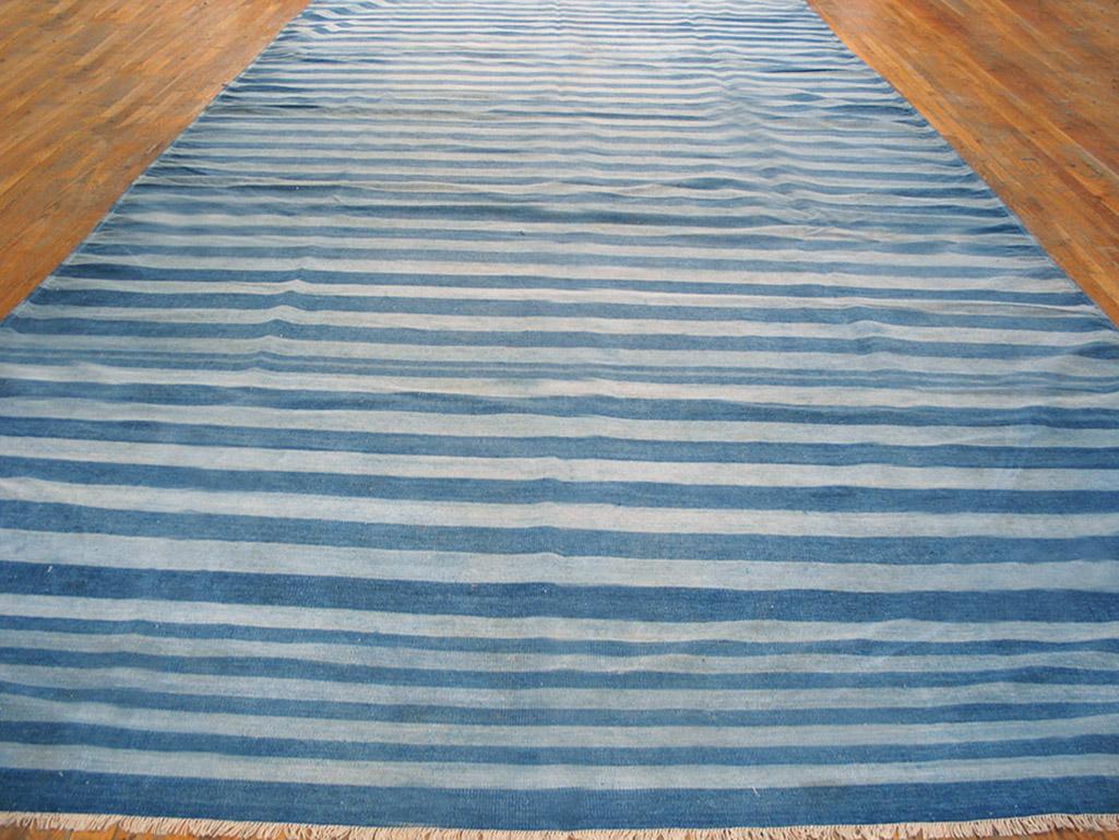 This all-cotton Indian Kilim-weave gallery format Dhurrie has a faintly Caucasian/ NW Persian design air about it with a denim blue field displaying a concentric lozenge over-pattern of serrated ashiks in teal blue, salmon-rust, red and sand, within