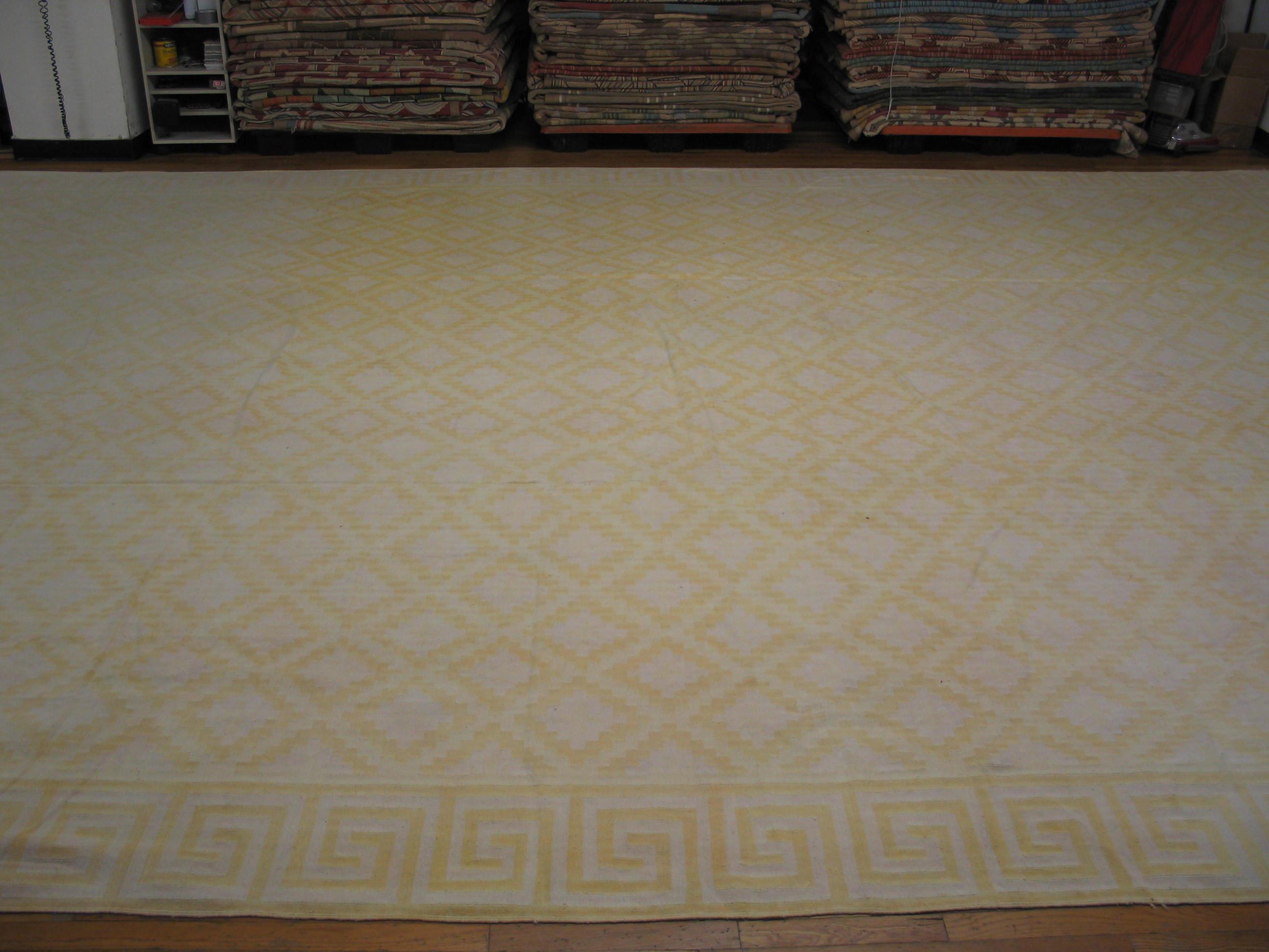 This giant all-cotton antique Indian flat-weave carpet shows a combination of two popular designs: a diaper of stepped diamonds within a conforming lattice, and a border employing a squared wave. The tonality is light, with light straw and cream.