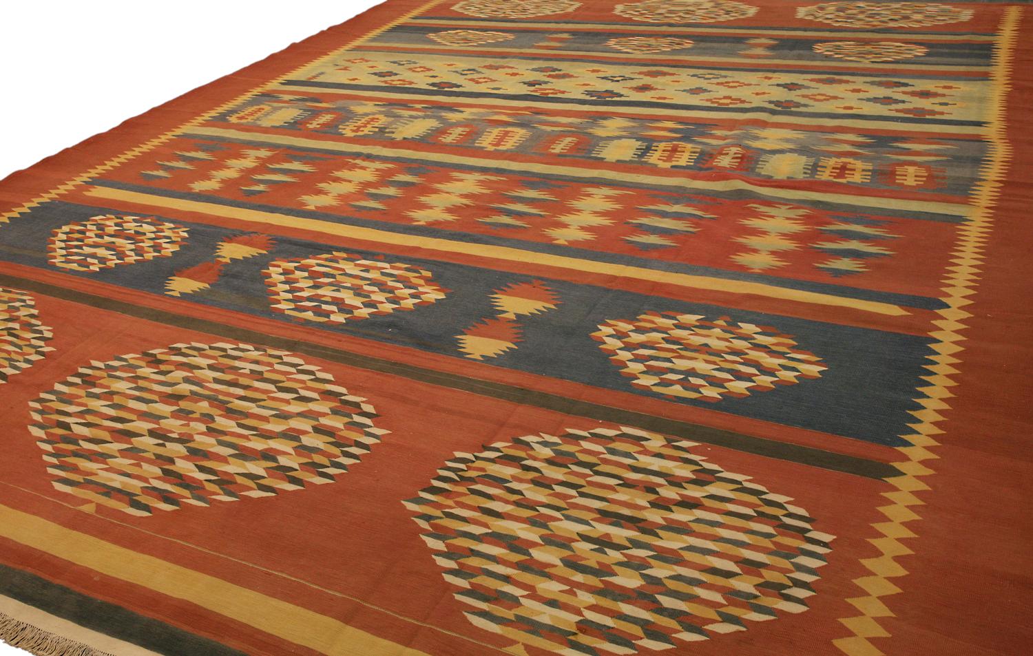 Dies ist ein antiker indischer Dhurrie-Kelim, der im ersten Viertel des 20. Jahrhunderts um 1920 gewebt wurde und 455 x 337 cm groß ist. Dieser Kelim hat ein geometrisches All-Over-Muster mit sieben Reihen von sich abwechselnden Motiven. Die Farben,