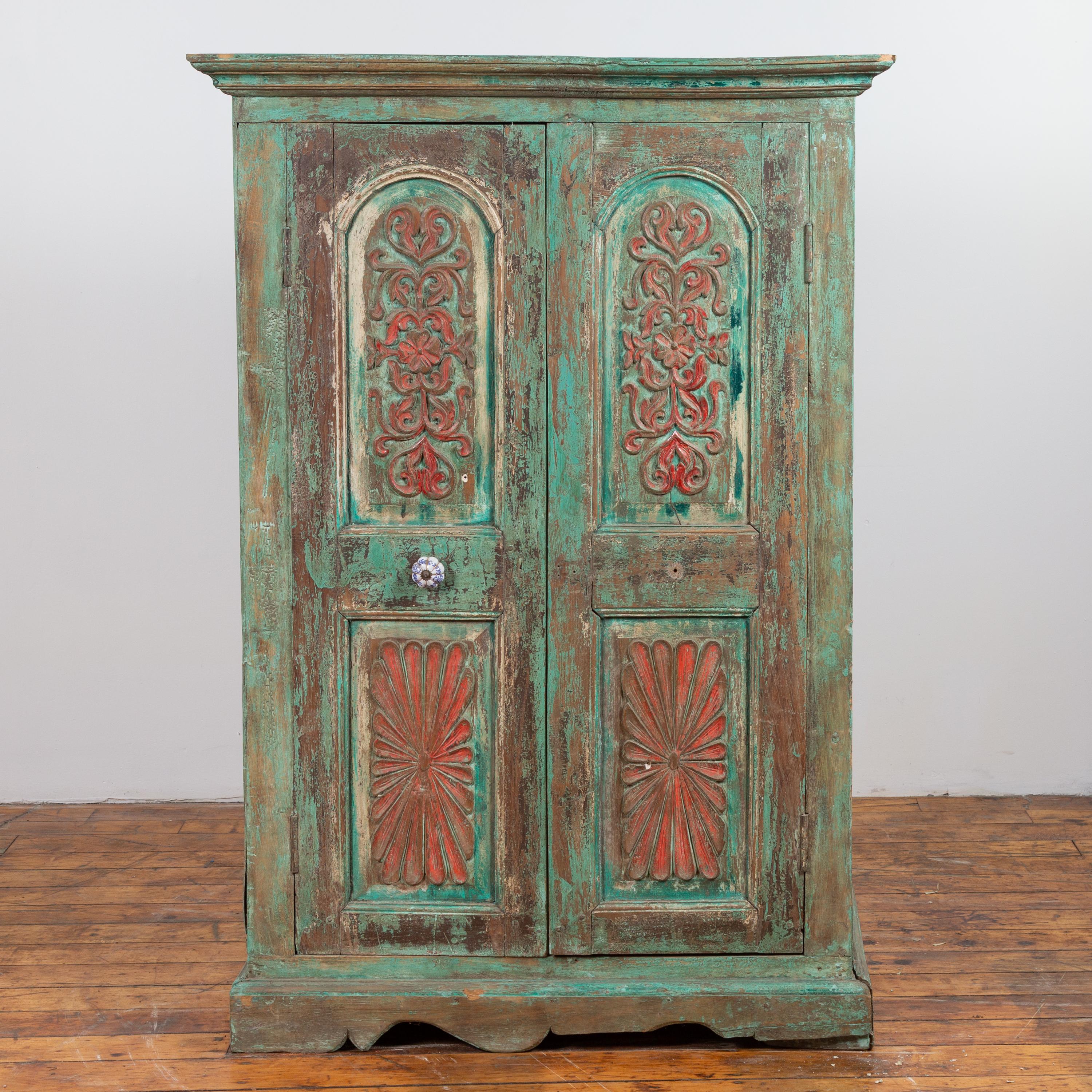 An Indian distressed green painted wooden wardrobe cabinet from the 20th century, with red accents, scrollwork and radiating motifs. Born in India during the 20th century, this charming wooden tall cabinet features a molded cornice, overhanging two