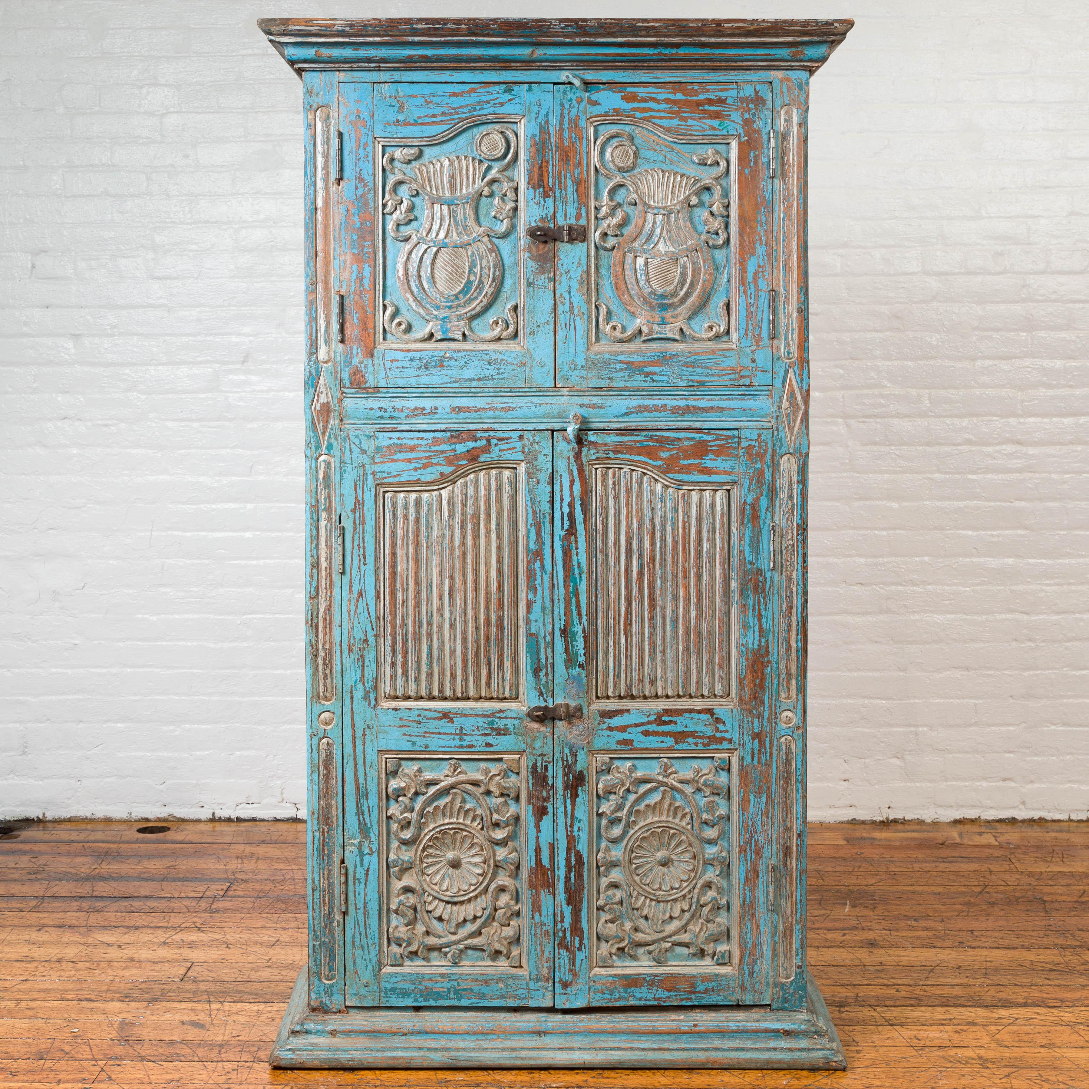 An antique Indian two-section blue painted wooden cabinet with carved panels. Featuring a tall silhouette and a hand-rubbed blue painted finish showing a nicely weathered appearance, this tall cabinet is made of two sections. A beveled cornice sits