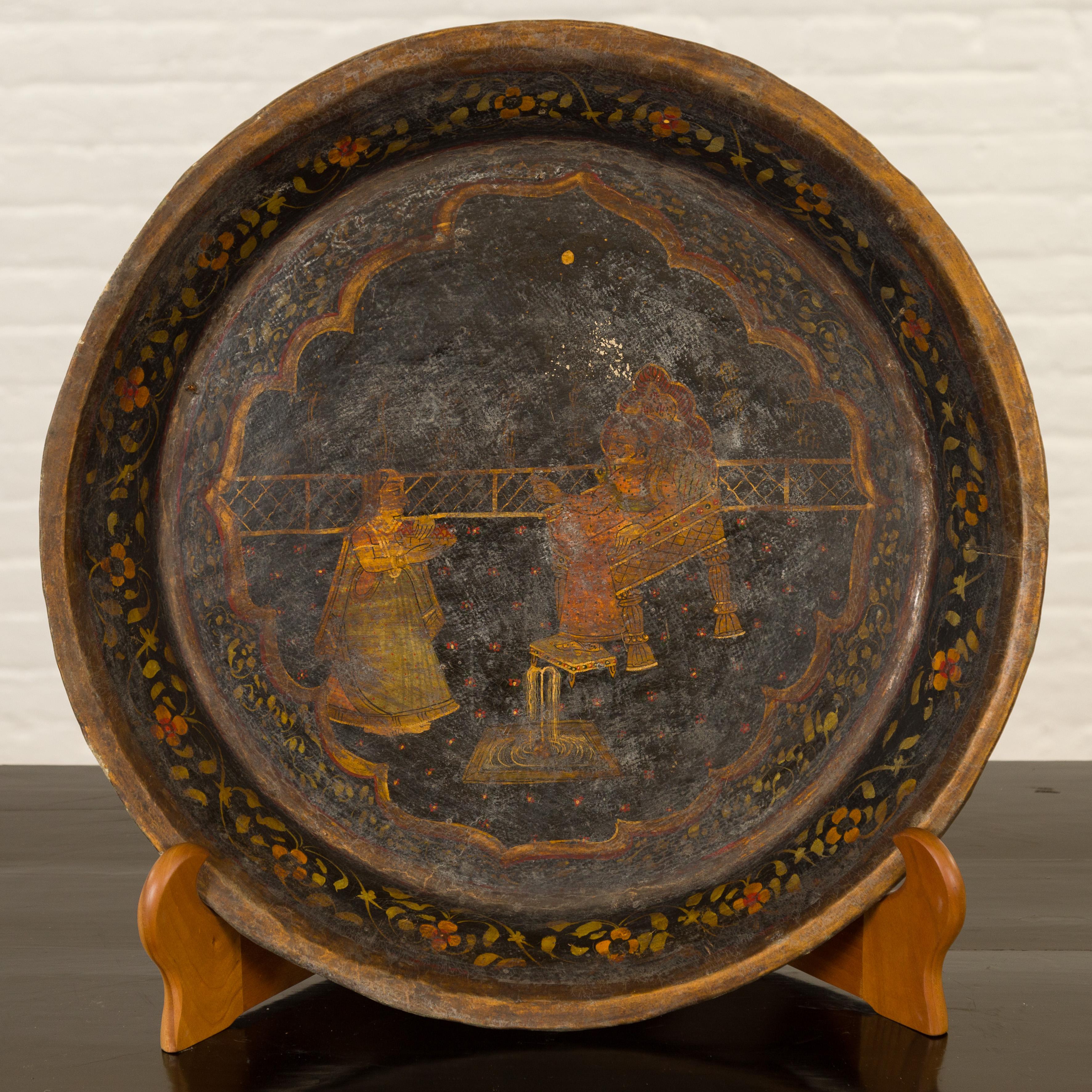 This antique Indian market tray from the 19th century captivates with its Mughal-inspired hand-painted décor. Created in India, the tray showcases two characters rendered in three-quarter profile, their delicate golden and earthy tones standing out