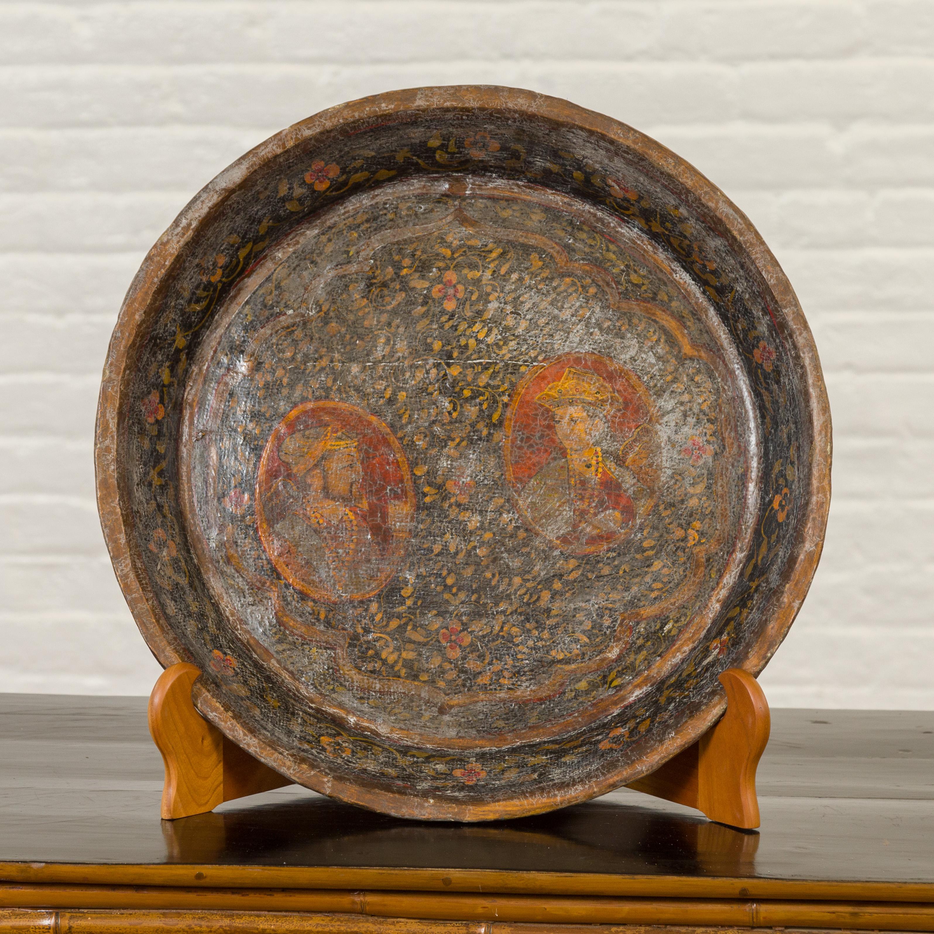 An antique Indian market tray from the 19th century, with Mughal inspired hand painted decor. Created in India, this market tray features a Mughal inspired hand painted decor depicting two portraits each in a medallion and surrounded by abundant