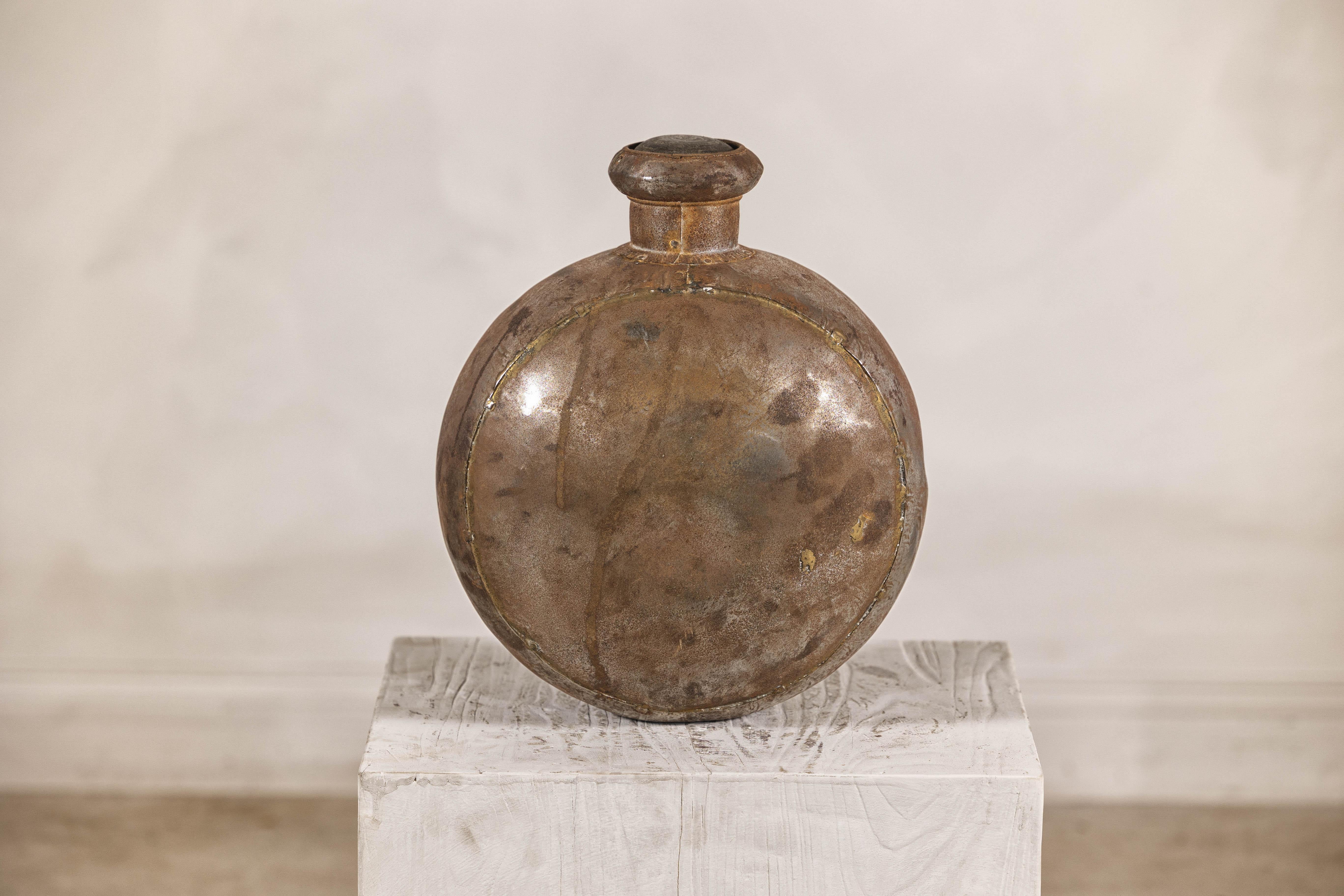 An Indian surahi water vessel with weathered patina. This early 20th-century Indian surahi—a traditional water vessel—showcases the enduring craftsmanship of Indian metalwork, offering both historical significance and decorative charm. Hand-forged