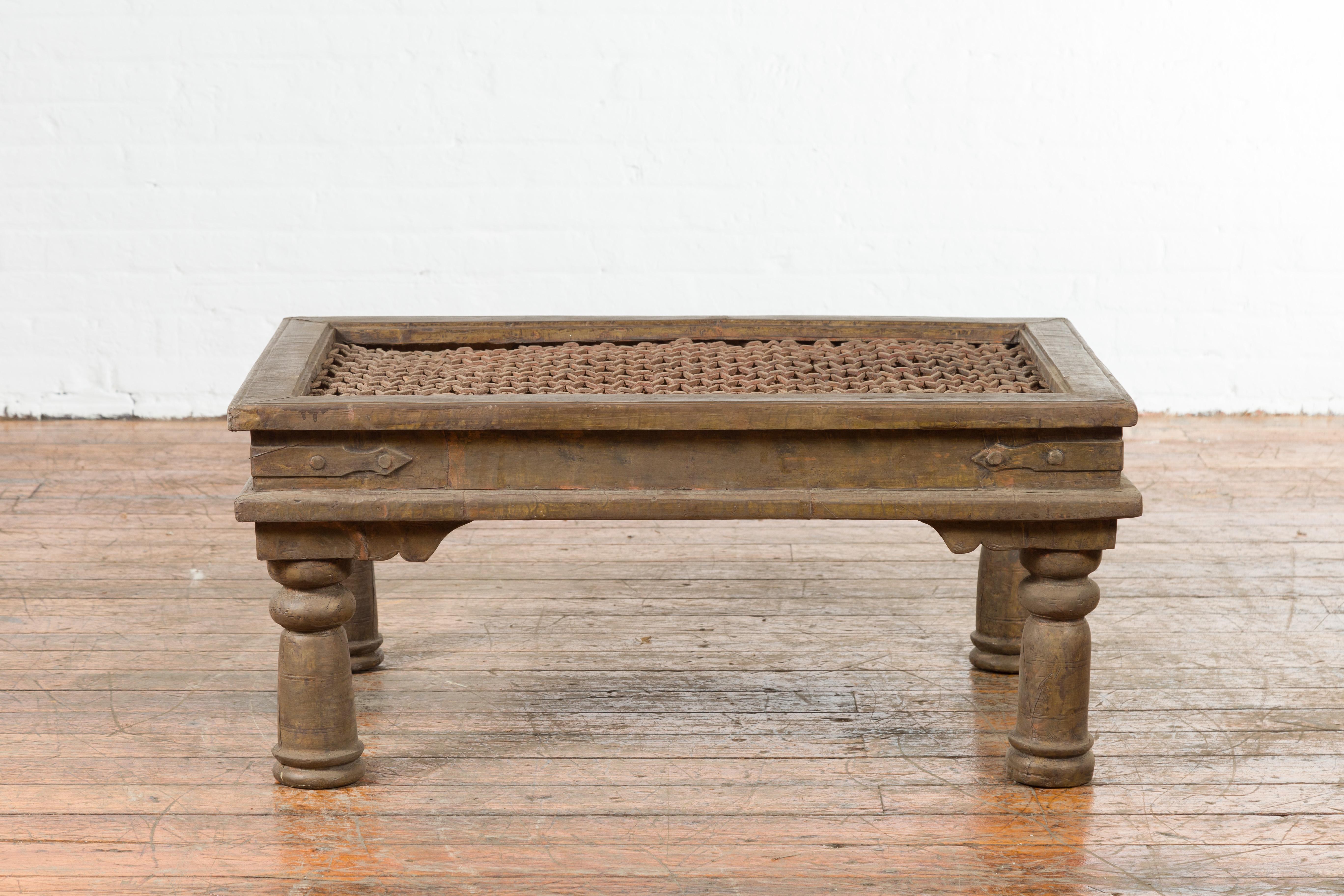 An Indian metal coffee table made of an antique brass window grill with iron geometric design top. Created in India during the early years of the 20th century, this Indian window grill with geometric patterns is resting on four turned baluster-type