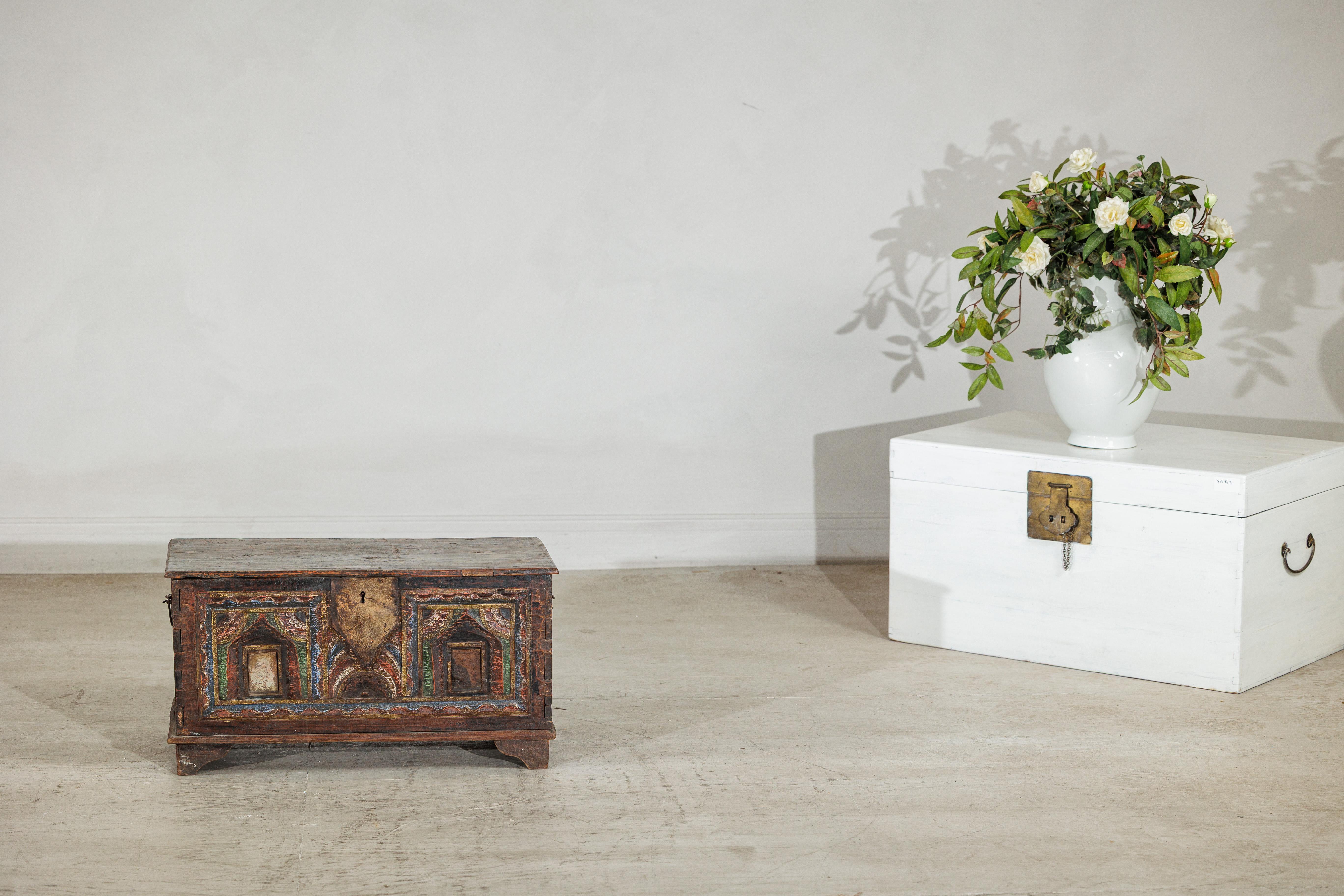 Ce coffre indien ancien, datant du XIXe siècle, capture le charme de l'artisanat régional avec sa façade richement peinte et ses détails architecturaux. Reposant sur de courts pieds en console, le coffre est surmonté d'un couvercle à charnière qui