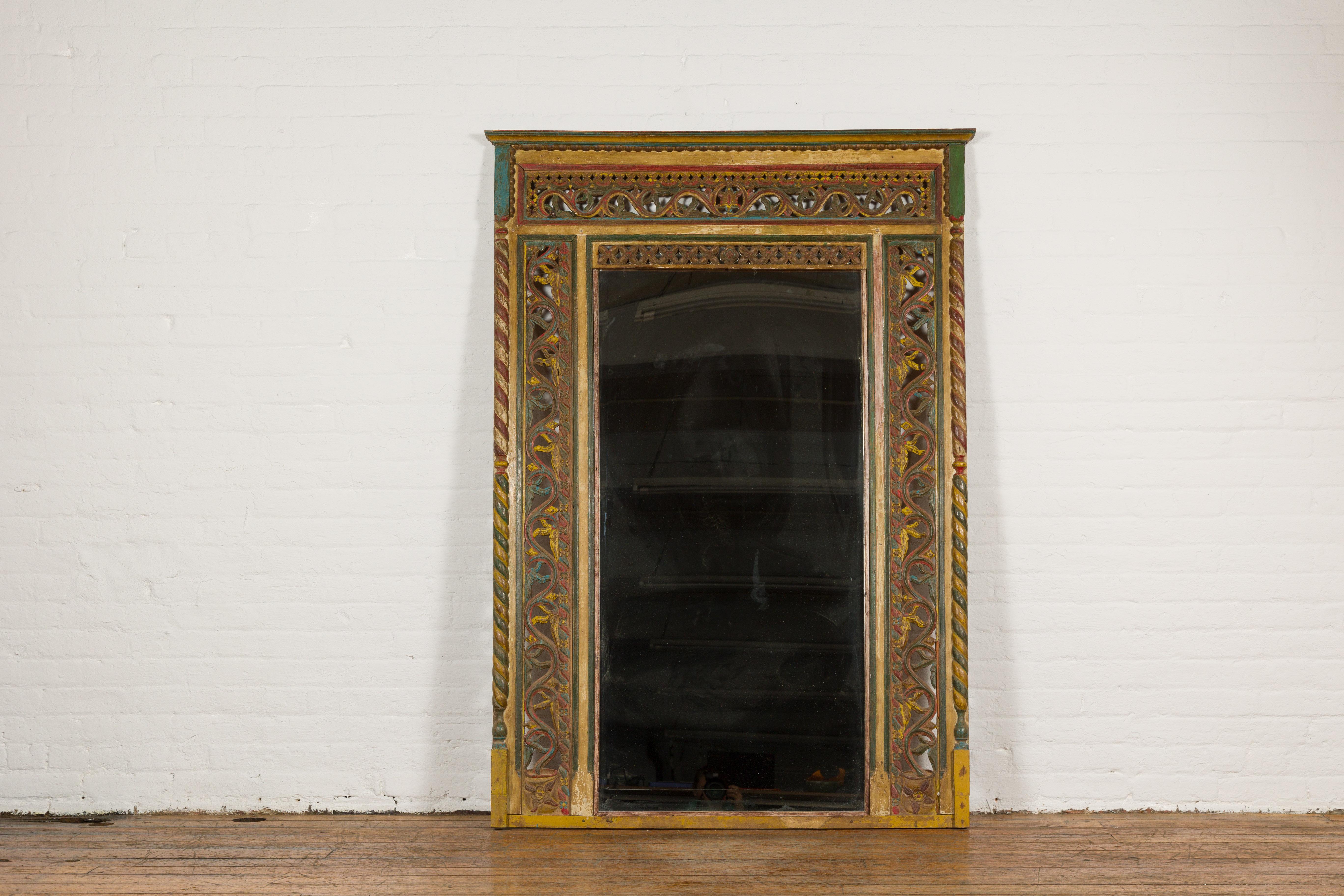 An antique Indian richly carved green, red and yellow painted window made into a trumeau mirror. Introducing a resplendent Indian trumeau mirror, masterfully repurposed from a beautifully carved and brightly painted window. This striking piece