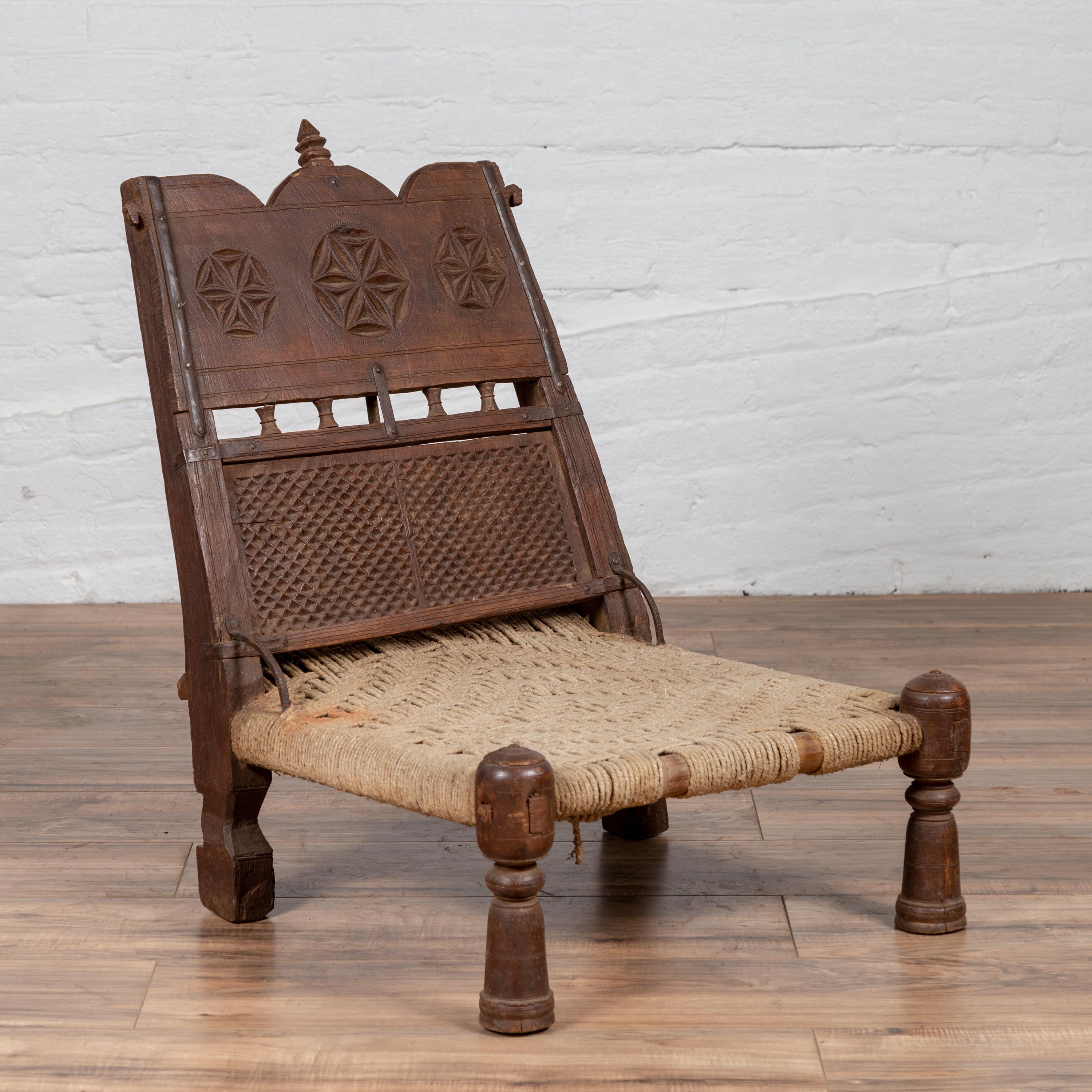 Une vieille chaise basse indienne en bois rustique du début du 20e siècle, avec de la ficelle tissée à la main et des motifs sculptés. Charmant notre regard par son aspect rustique, cette chaise basse en bois présente un court dossier incliné