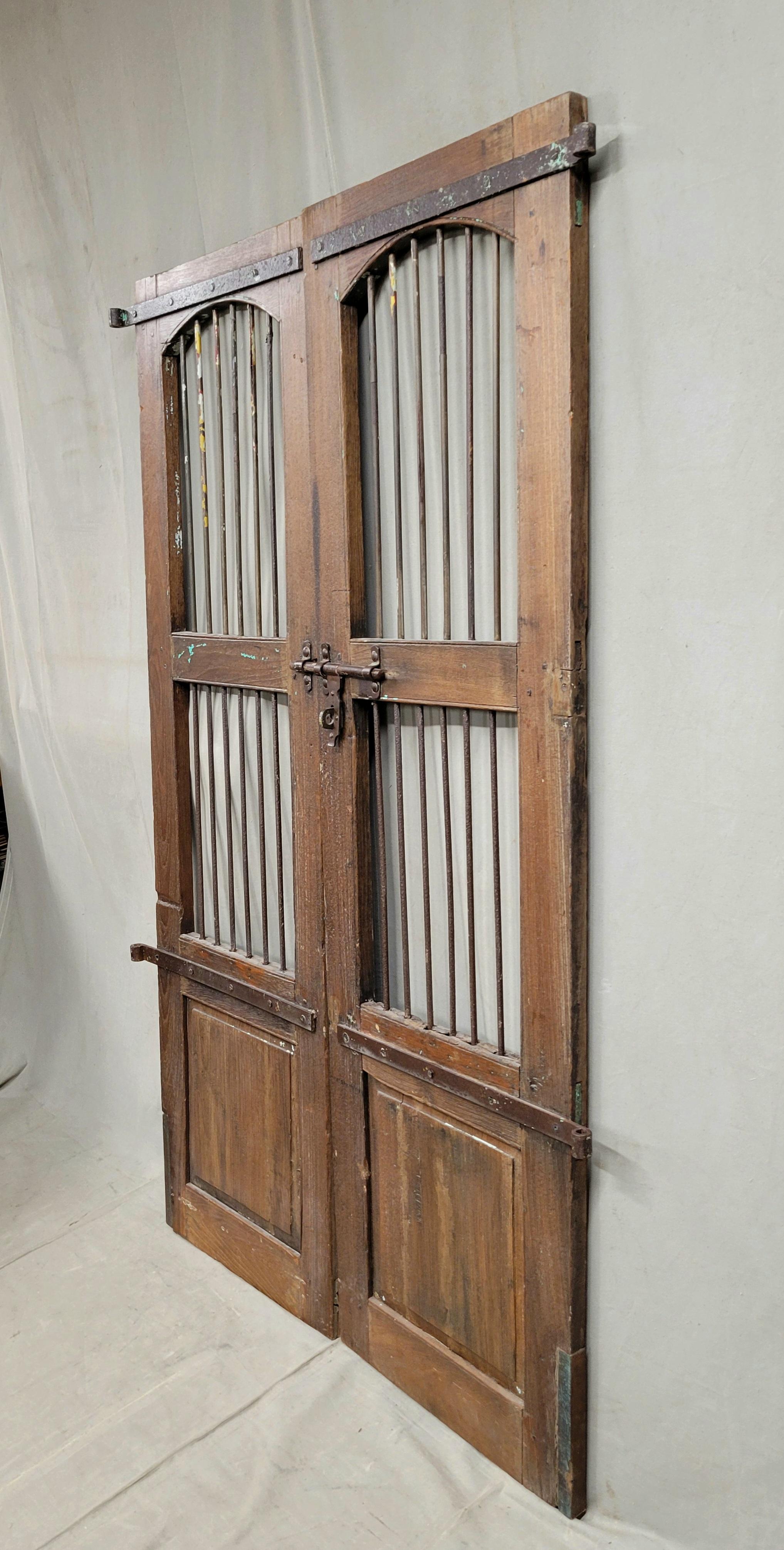 A beautiful set of antique Indian rustic teak and iron gates with old hardware intact. The old teak and original iron hardware lend a rustic feel. Also notice the remnants of old paint randomly overall. These gates could be used outside, as an entry