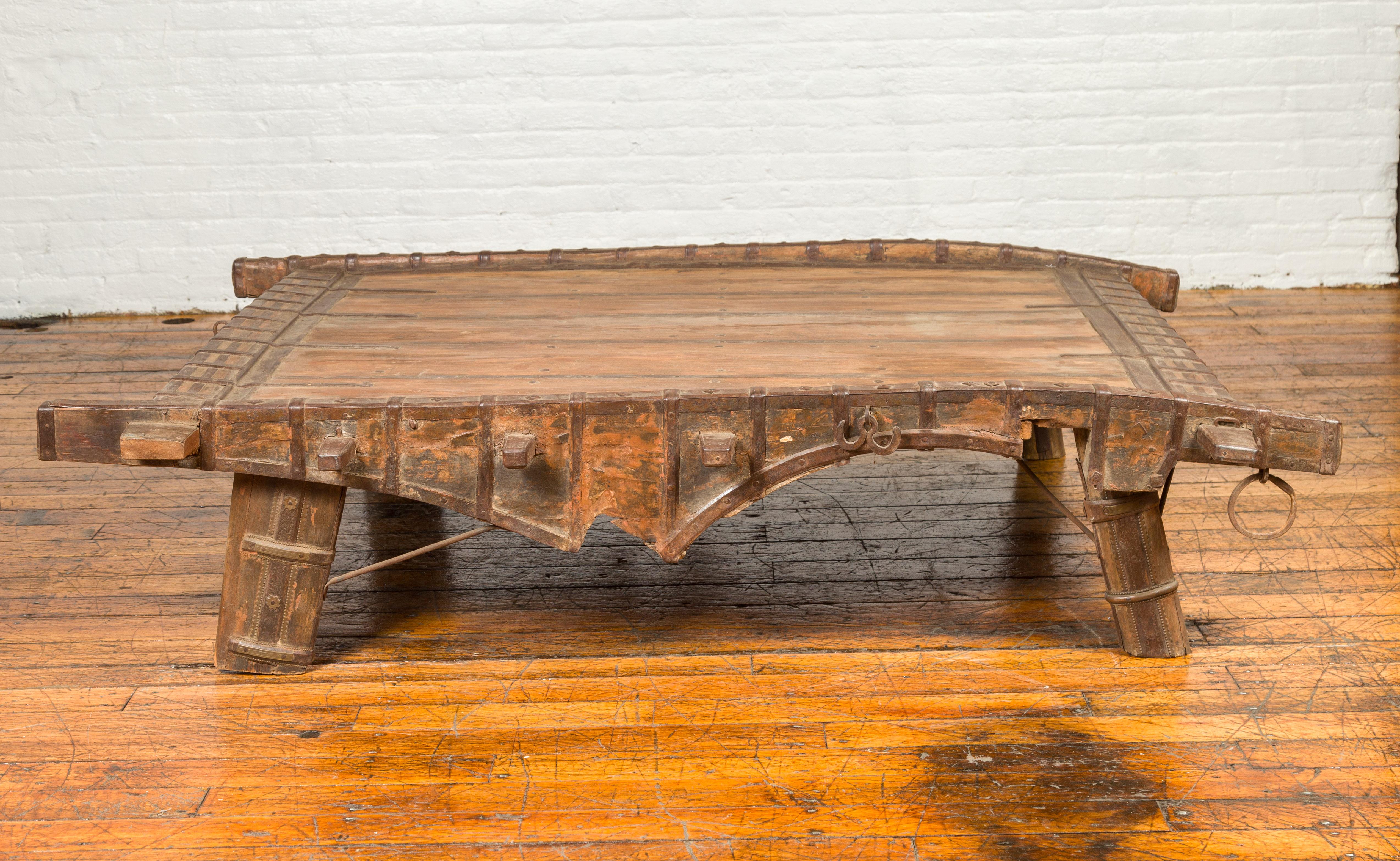 An Indian rustic wooden ox cart from the 19th century, made into a coffee table with uneven top and metal accents. Perfect to be used as a coffee table, this conversation piece is an old wooden ox cart accented with metal accents and raised on