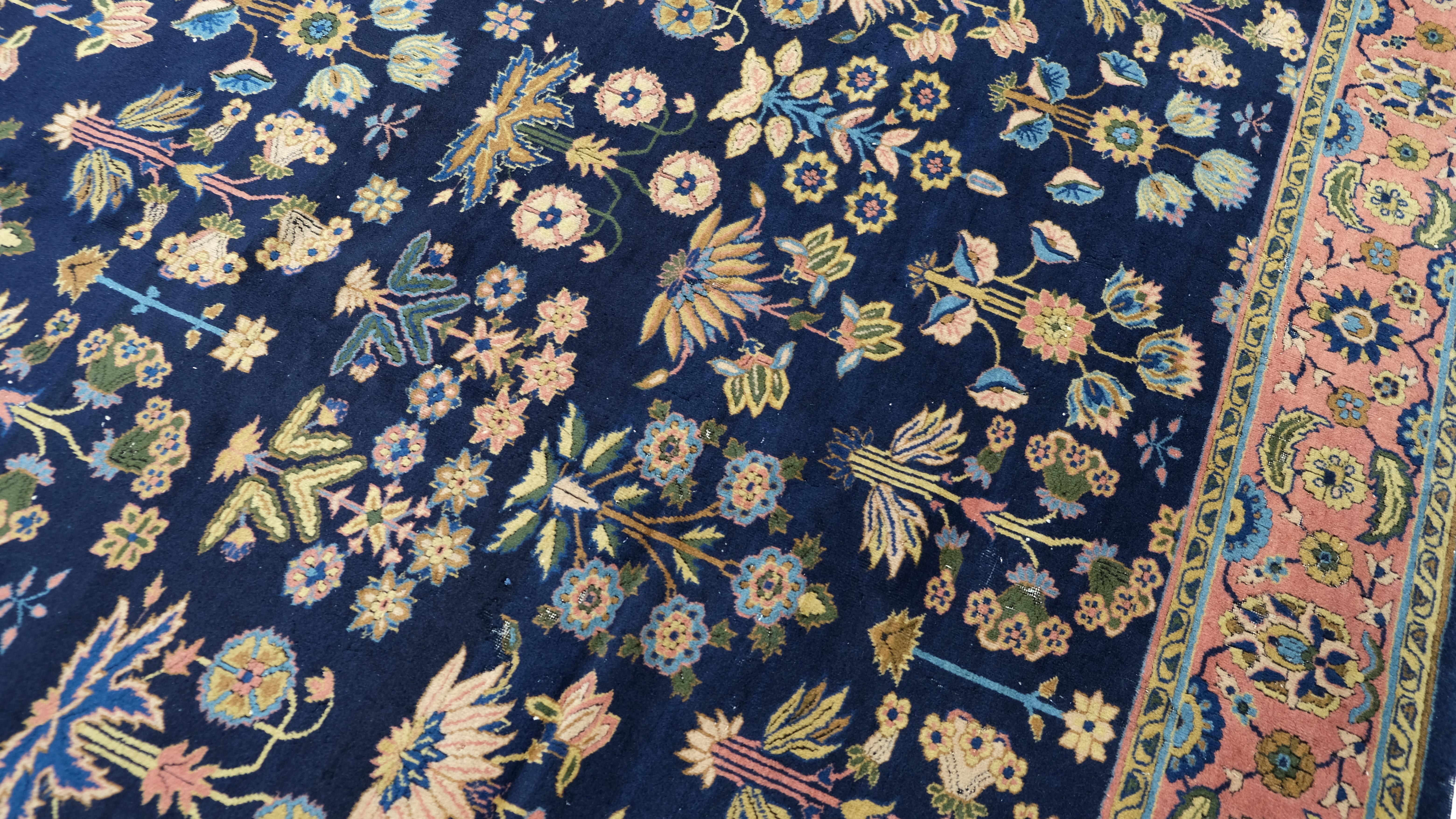 Rehaussez votre espace avec ce tapis antique exquis, fabriqué en Inde et inspiré de motifs traditionnels. Présentant un motif floral complexe sur un fond bleu marine profond, ce tapis est encadré par une bordure contrastée de couleur saumon, ornée