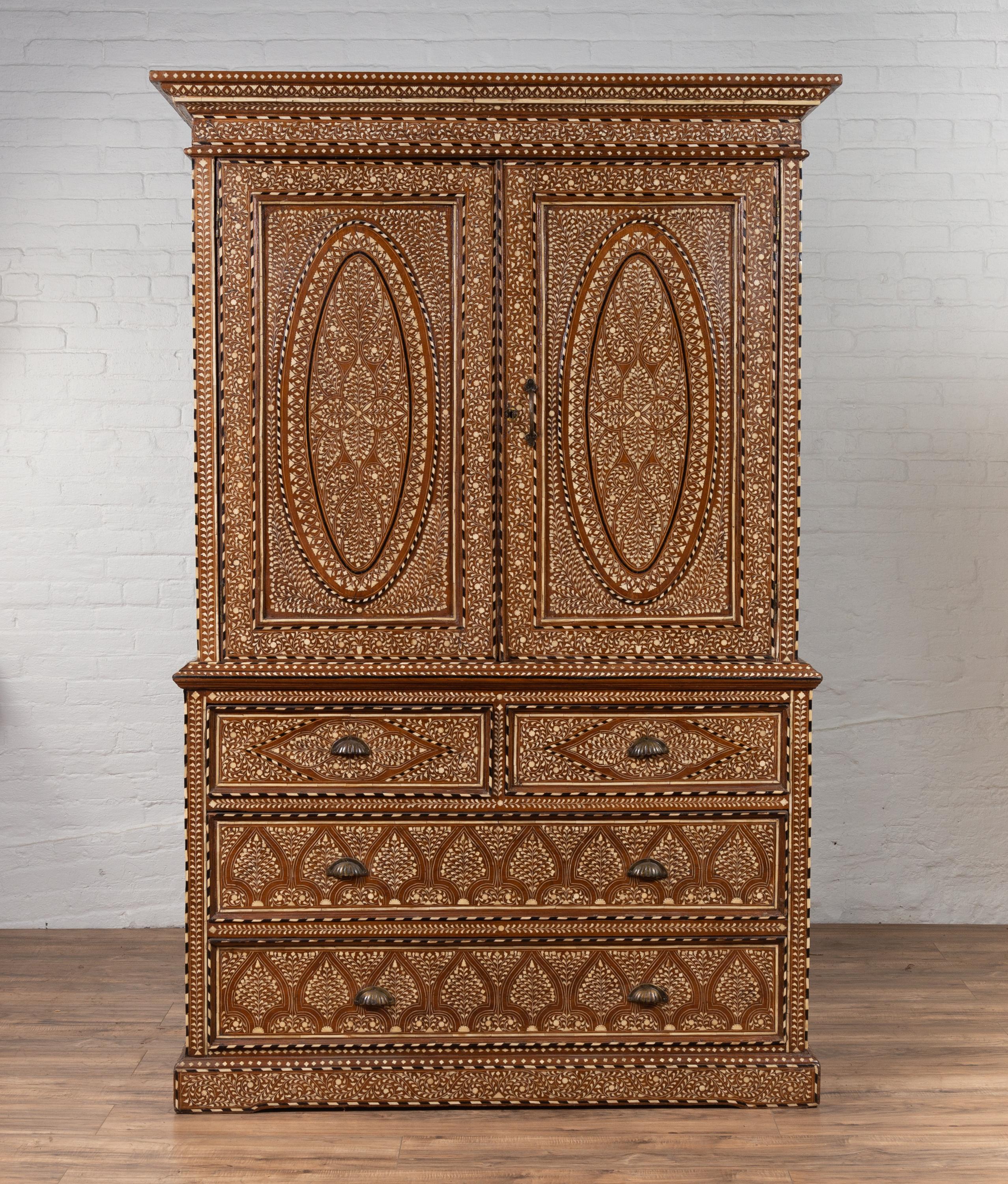 An antique Indian sheesham wood wardrobe cabinet from the early 20th century, with ebonized accents and bone inlay. Born in India during the early years of the 20th century, this stunning tall cabinet is adorned with an abundant décor of foliage and