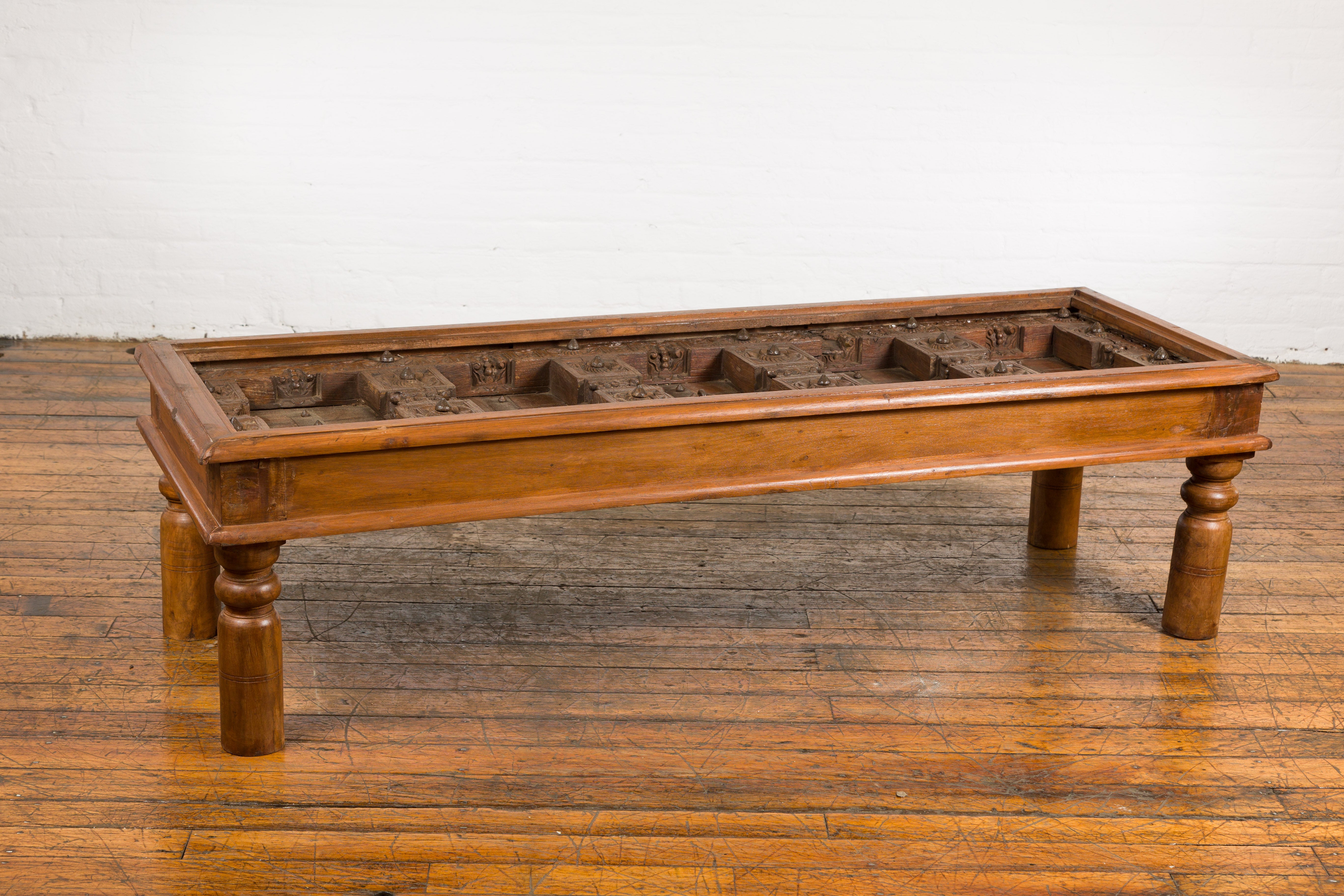 Une ancienne porte extérieure indienne transformée en table basse avec des détails en bois de sheesham et en fer. Embrassez la tapisserie opulente de l'héritage indien avec cette table basse spectaculaire, magistralement réutilisée à partir d'une