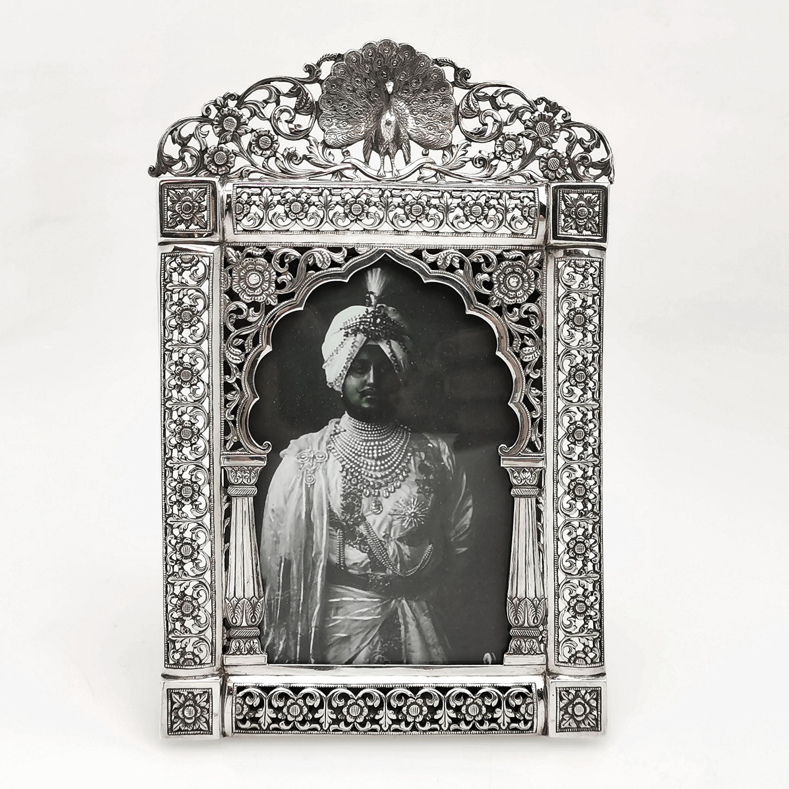A beautiful antique Indian silver photograph frame. This picture frame is embellished with a delicate chased and pierced design showing stylised flowers and topped with a peacock.

Made in Bhuj Kutch, India in circa 1880 by Oomersee