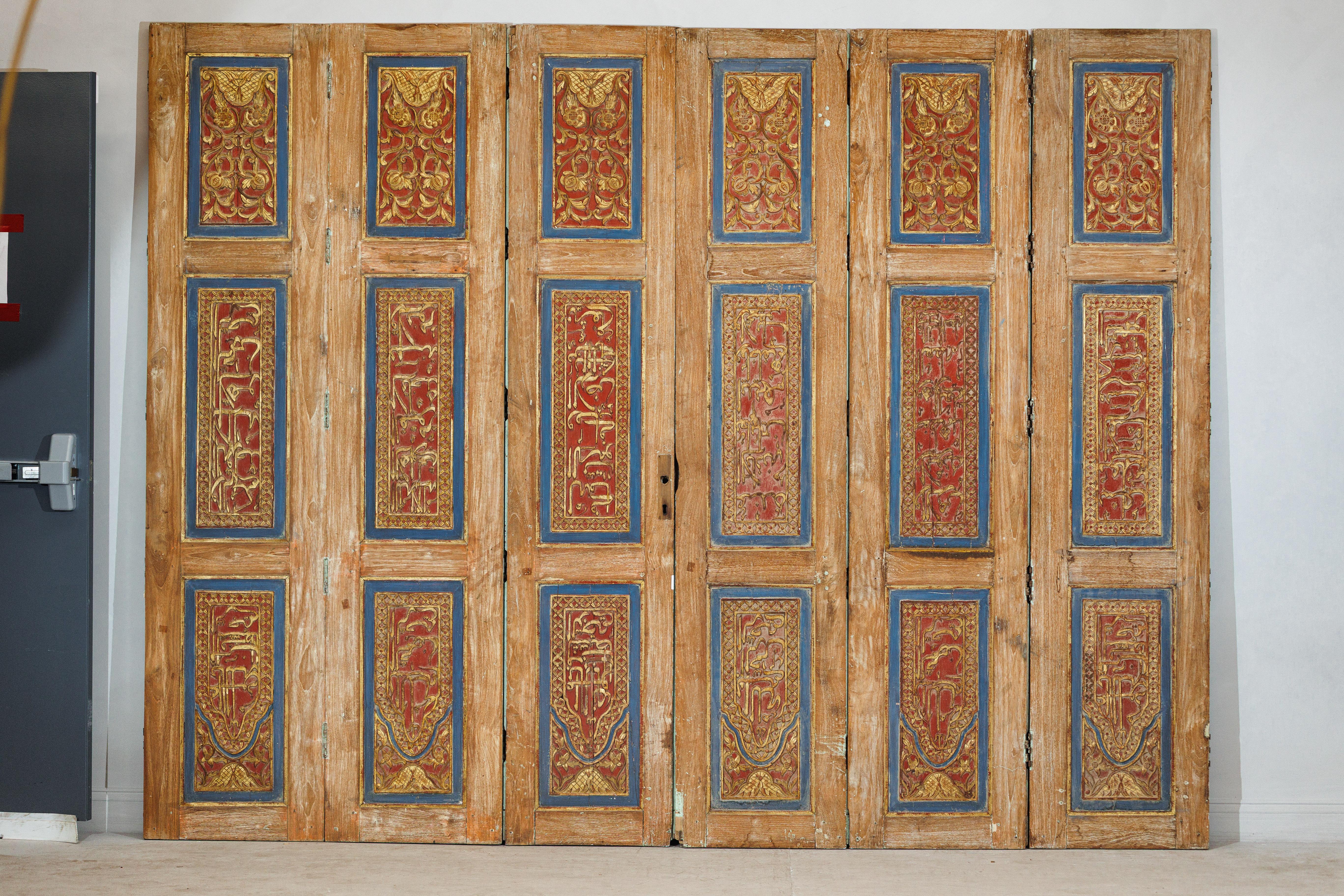 An antique Indian Anglo-Raj period, circa 1900 six-panel carved wooden screen featuring painted calligraphic inscriptions and floral motifs. Each tall, narrow panel - measuring 19
