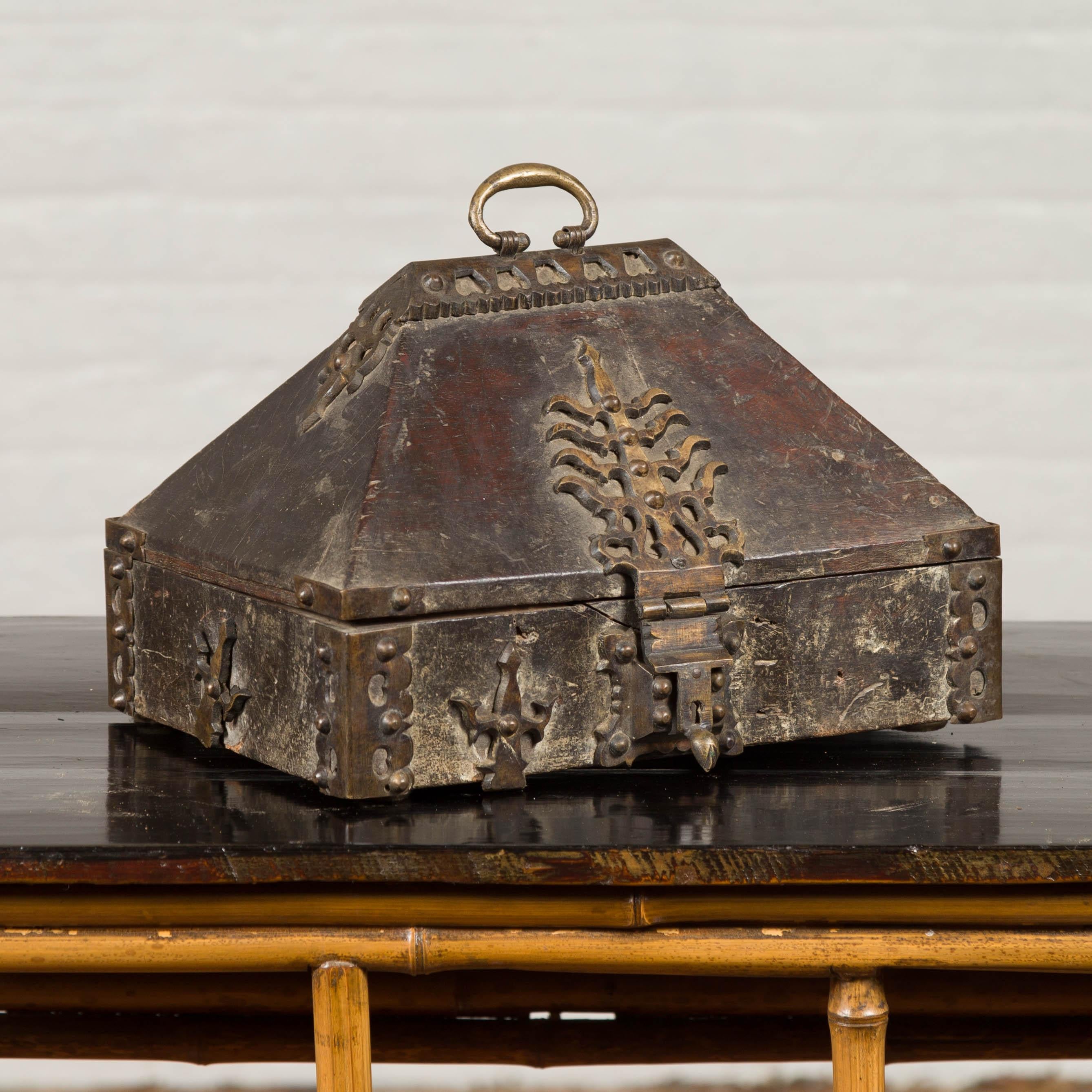 An unusual Indian antique treasure box used as a merchant's chest with iron decor and weathered patina. Our eye is immediately attracted to the lines and exquisite decor of this treasure box, adorned with iron motifs. A pyramidal lid topped with
